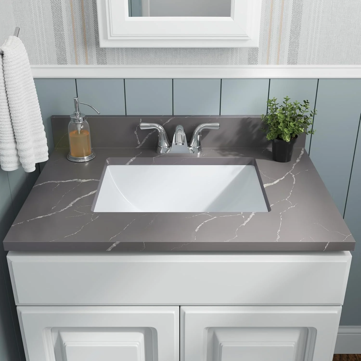 Bathroom vanity with marble countertop, white sink, chrome faucet, soap dispenser, green potted plant, and a mirror above.