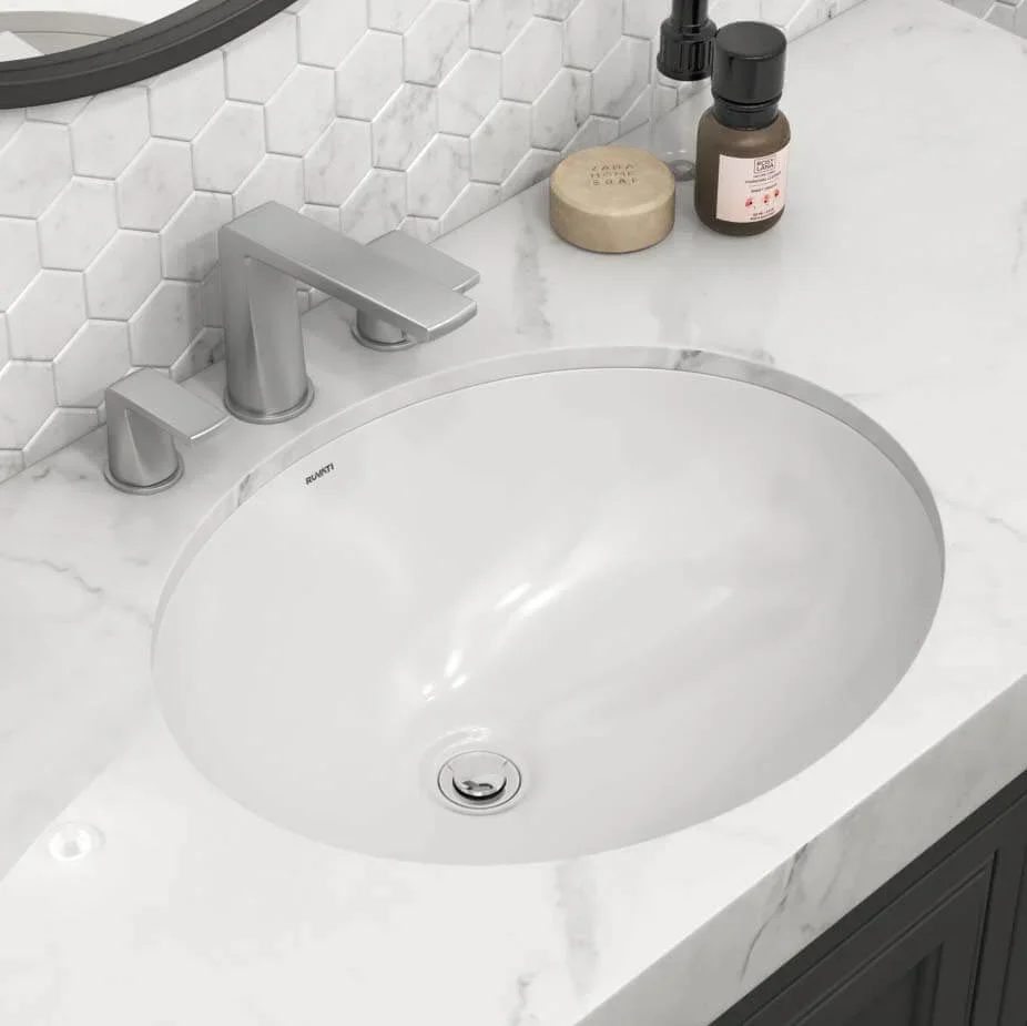 Bathroom sink with silver faucet, soap, and lotion bottles on a white marble countertop. White hexagonal tile backsplash.