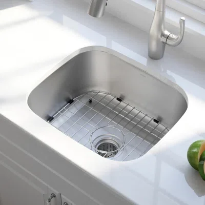 Kitchen sink with a stainless steel basin and a wire rack inside, alongside a green apple on the countertop.