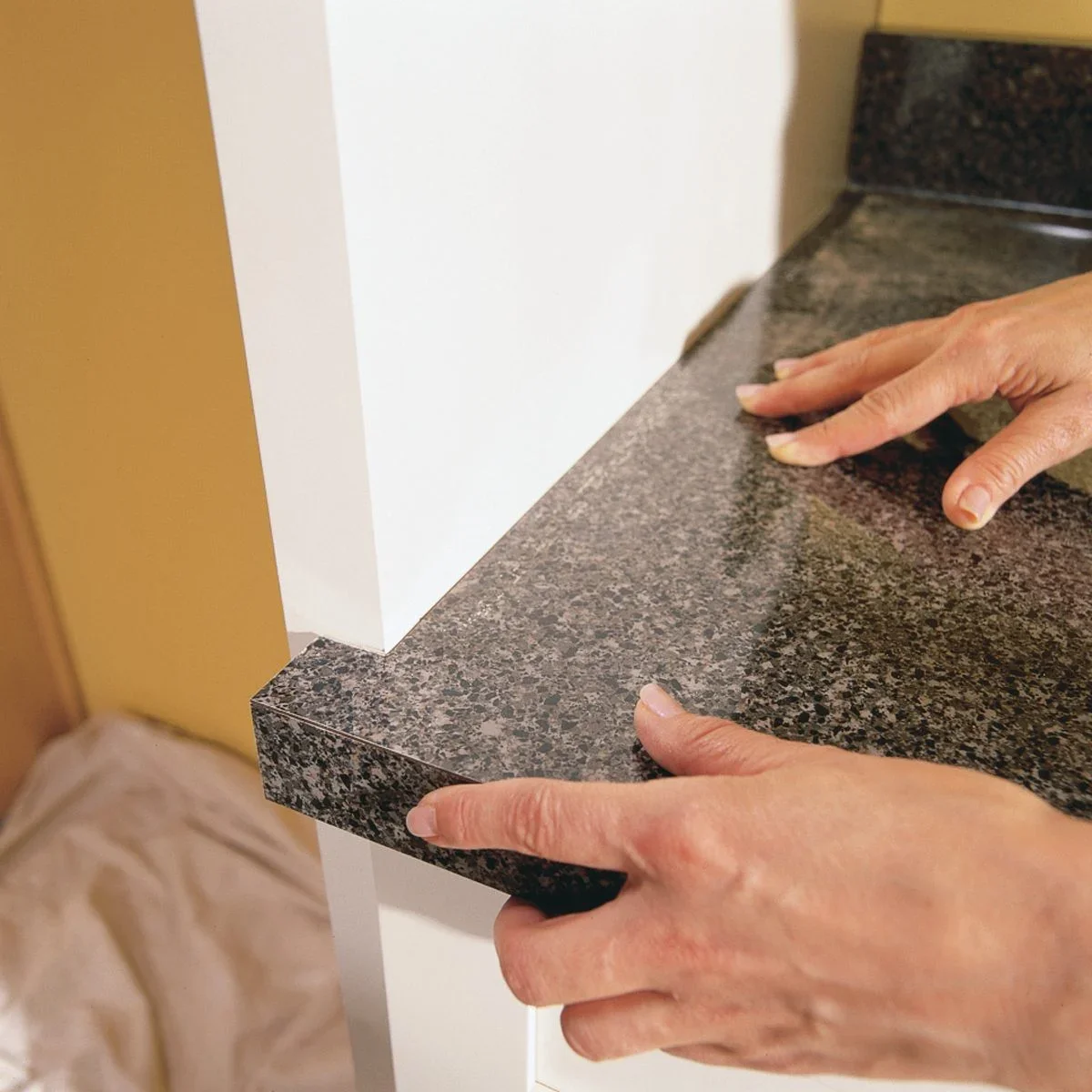 Person placing a black granite countertop on a white kitchen cabinet.