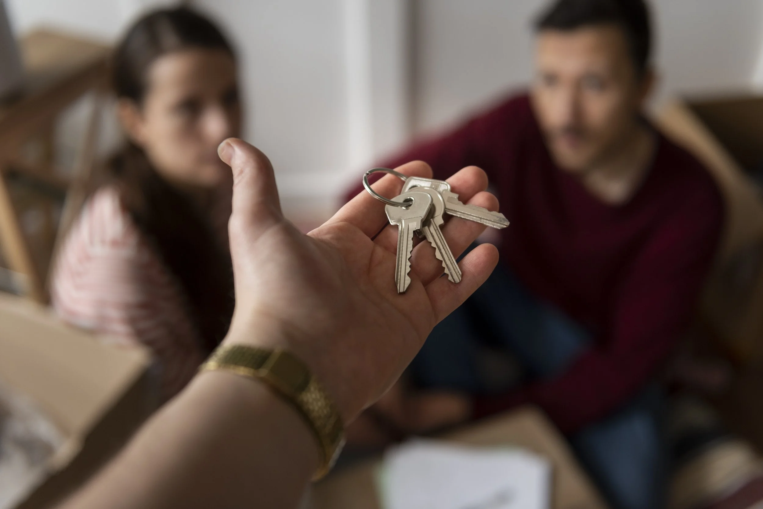 Person holding a set of keys, with a woman and a man in the background.