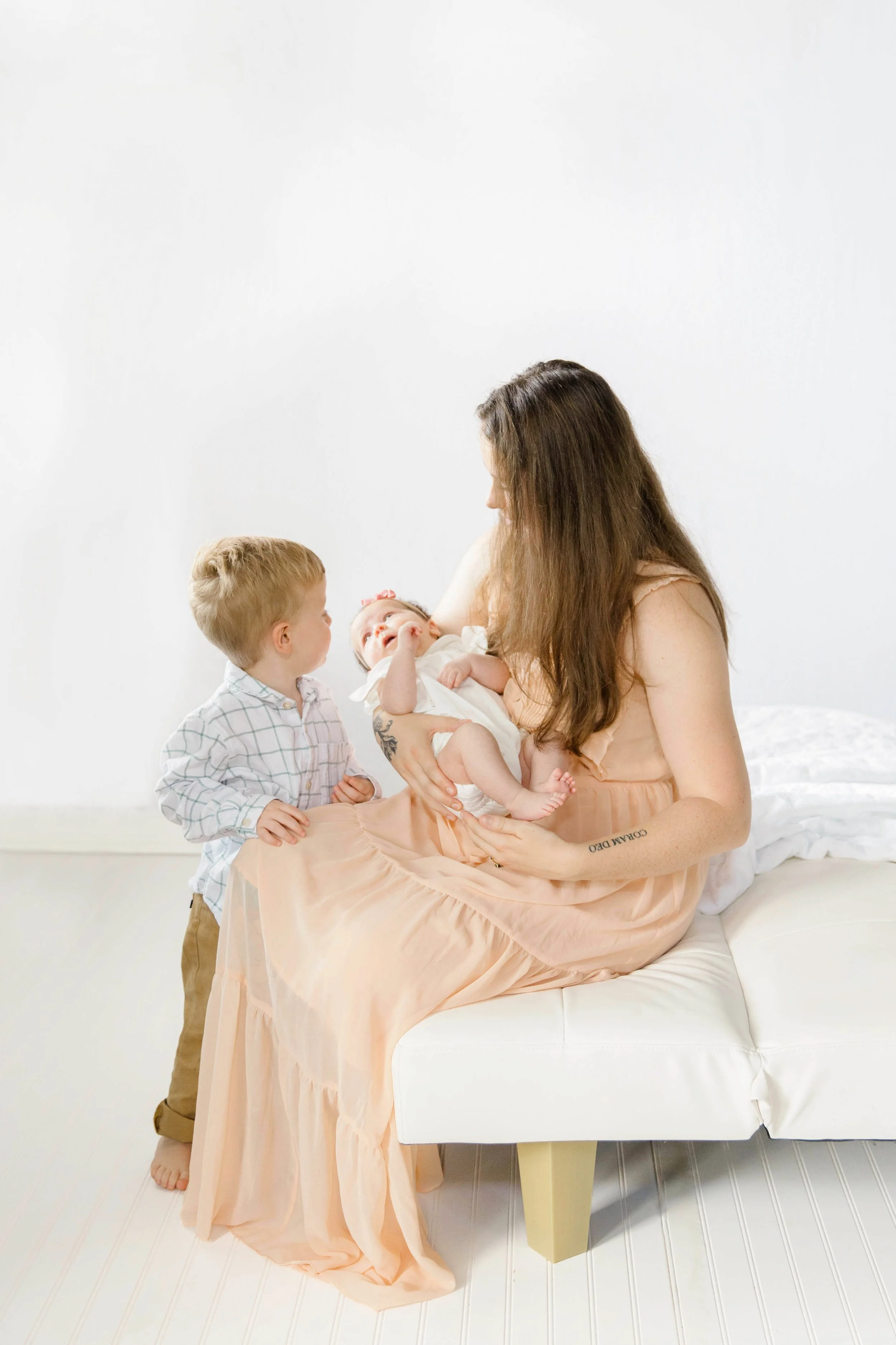 mother holding baby with toddler looking on