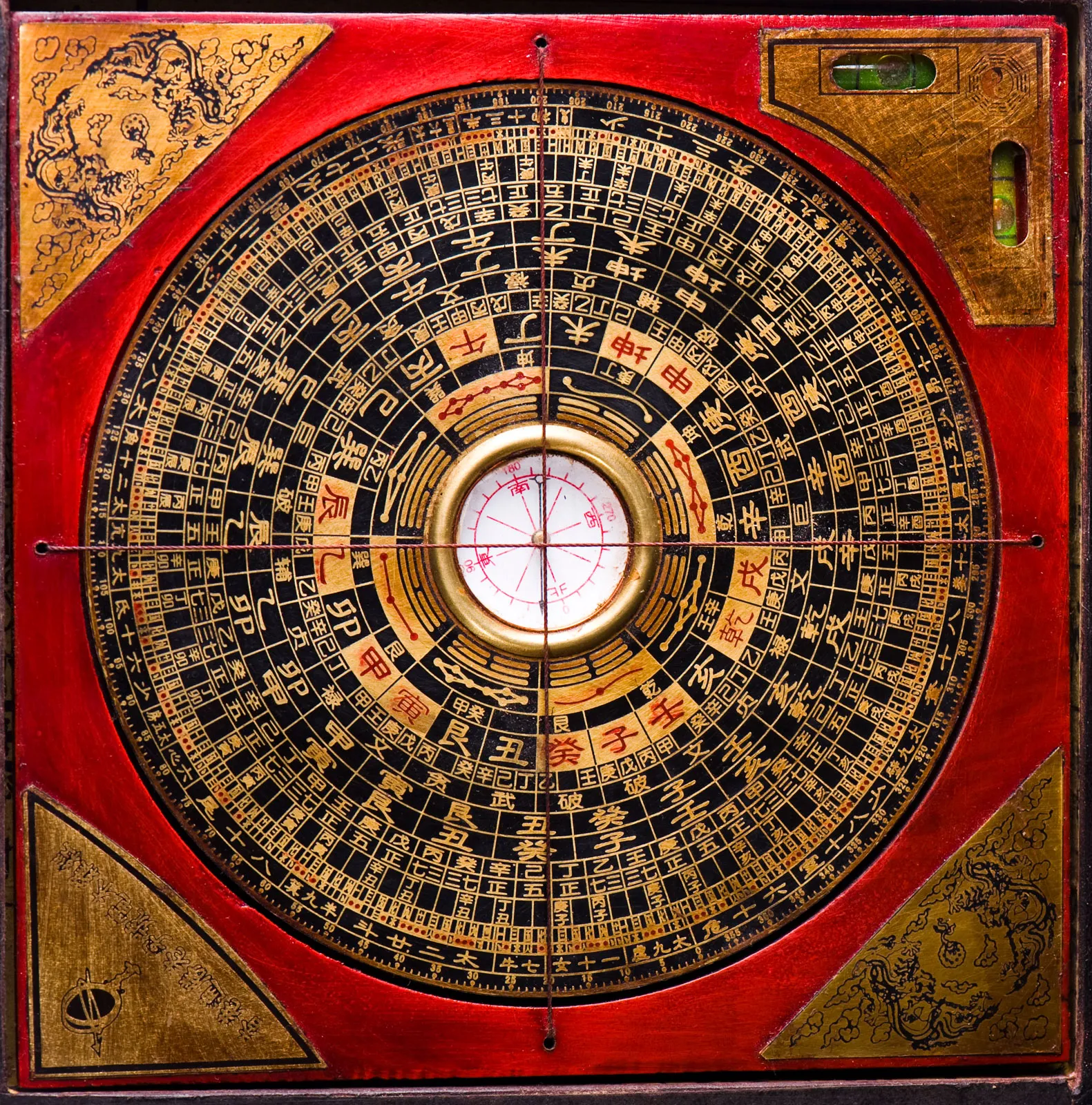 A traditional Chinese Luo Pan compass with a red border and intricate black and gold markings, featuring Chinese characters and symbols arranged in concentric circles.