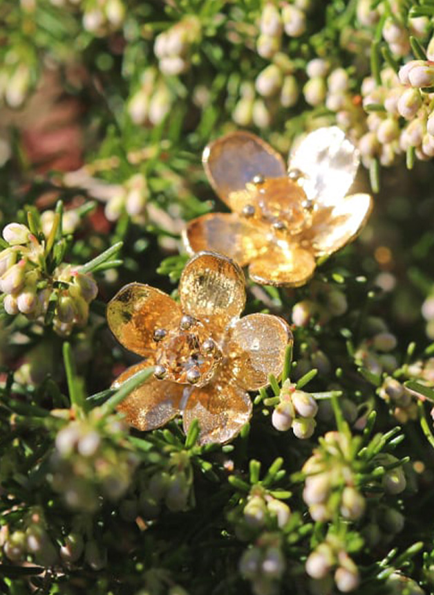 Decorative gold flower-shaped jewelry amid green foliage and small white flowers.