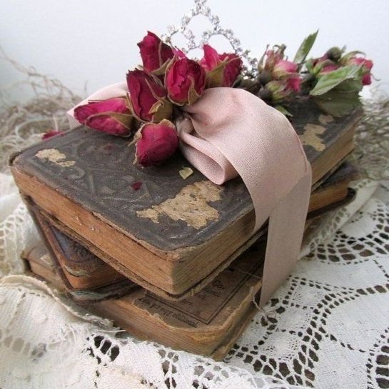 Old, worn books with dried pink roses, a pink ribbon, and lace fabric.
