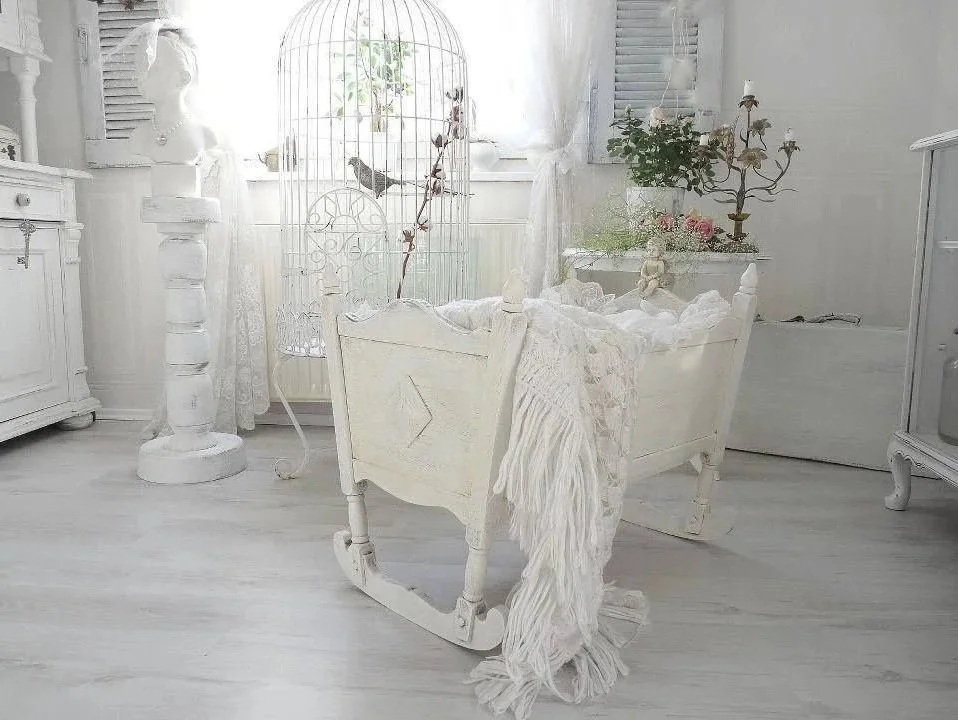 An all-white room with vintage furniture, a birdcage with birds inside, and decorative elements like a bust sculpture and a candelabrum.