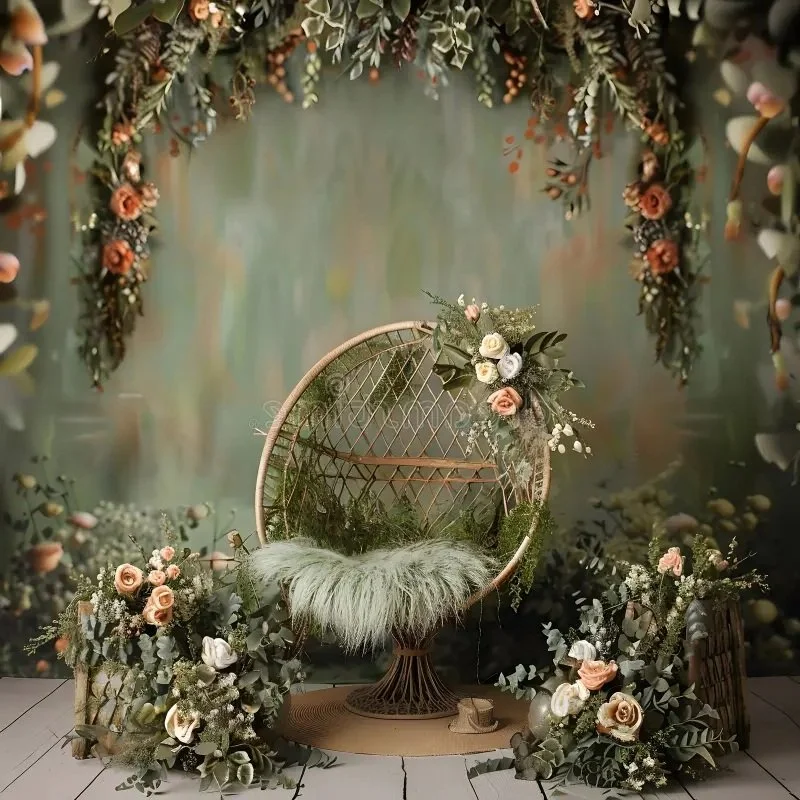 Decorative setup with a wicker circular chair adorned with floral arrangements, green foliage, and a fluffy cushion, surrounded by additional floral and greenery arrangements, with a blurred green-toned backdrop.