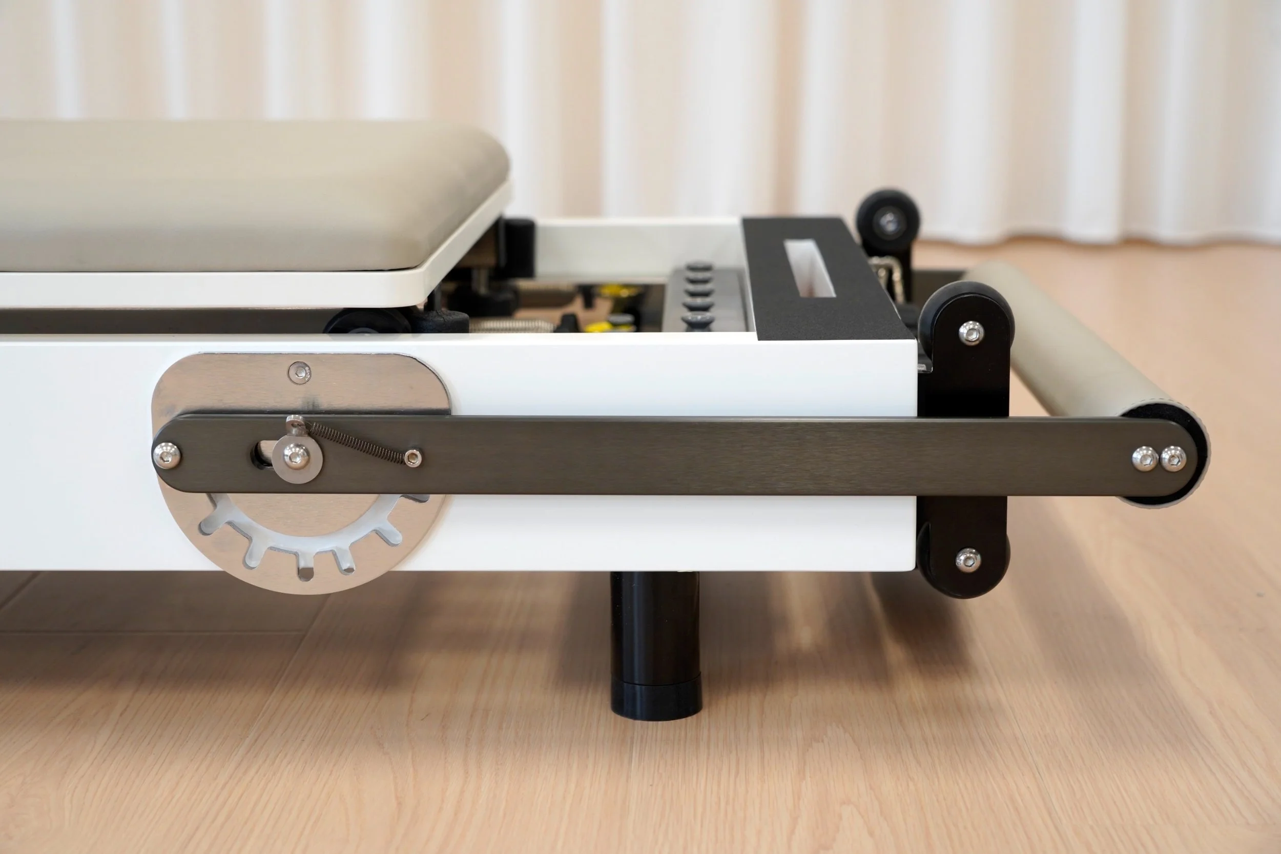 Close-up image of a mechanical bed or hospital cot with wheels, metal parts, and adjustable components on a wooden floor.