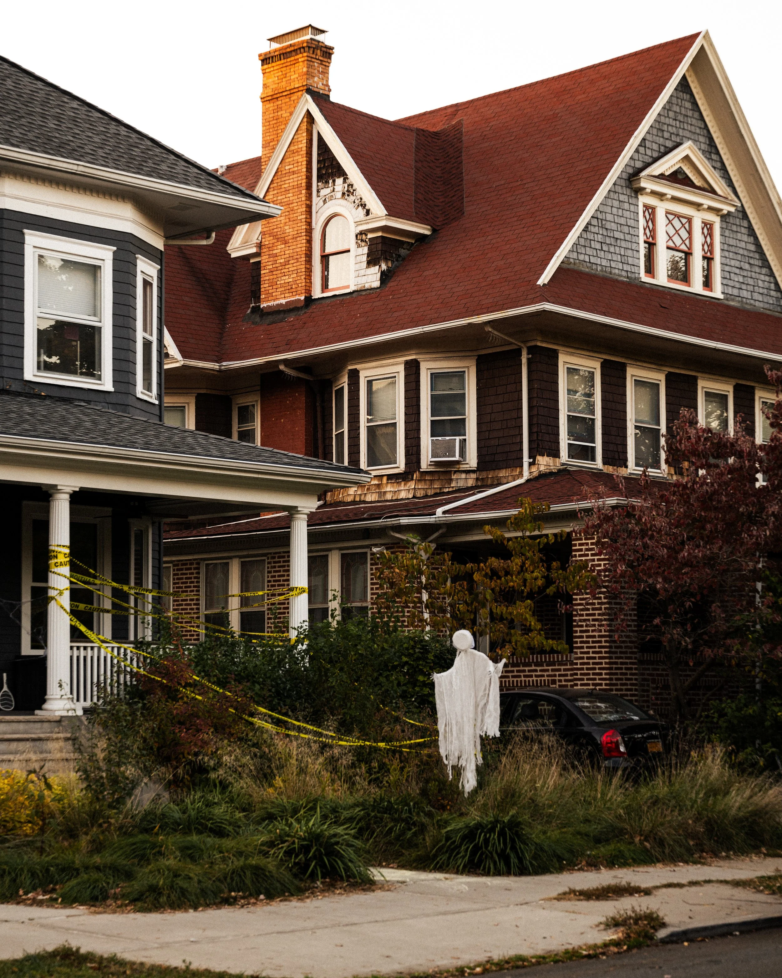 Haunted house decorated for Halloween with white ghost figure, caution tape, and fallen leaves in the yard.