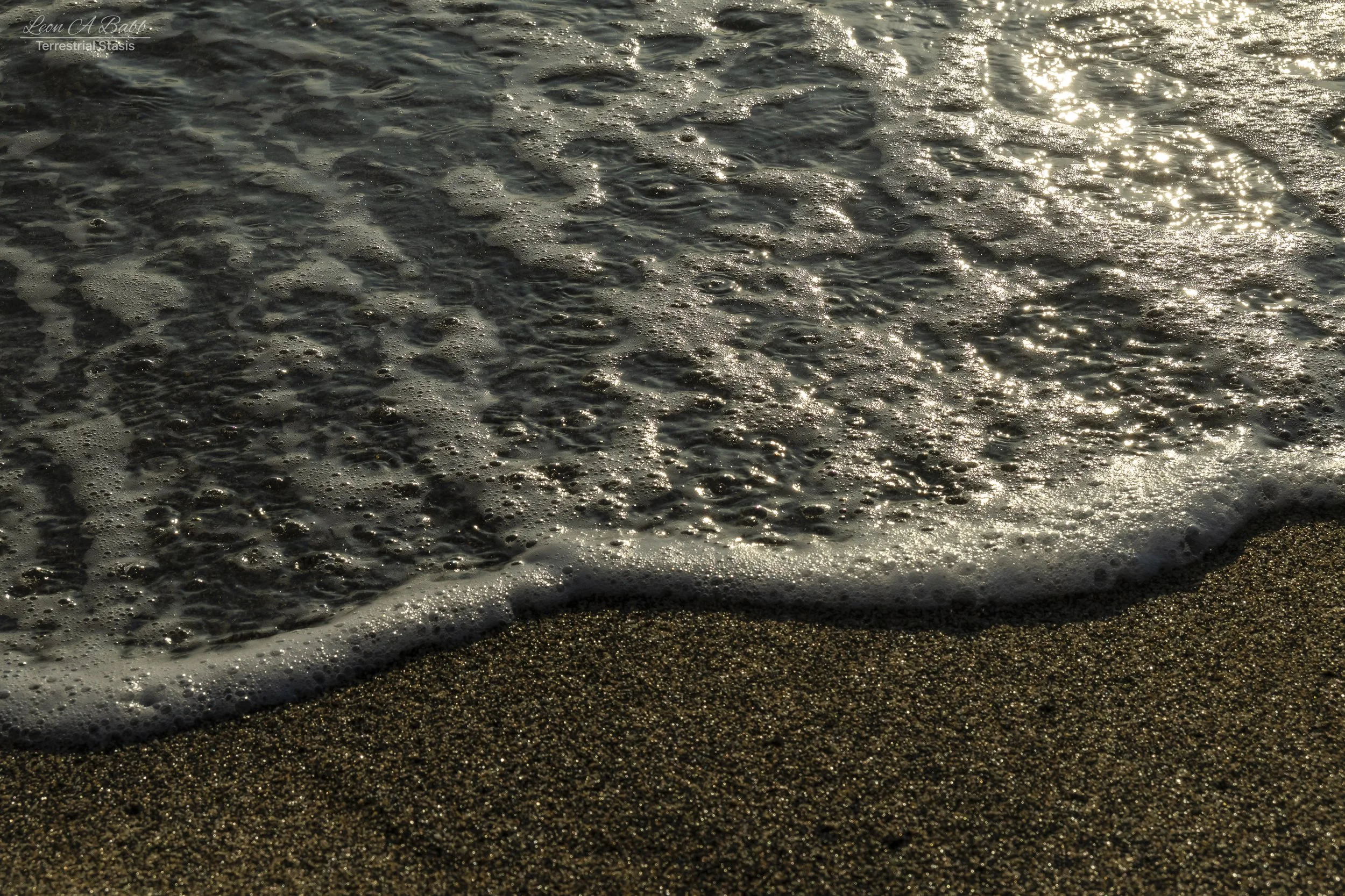 Close-up of gentle ocean waves lapping onto a sandy beach at sunset.