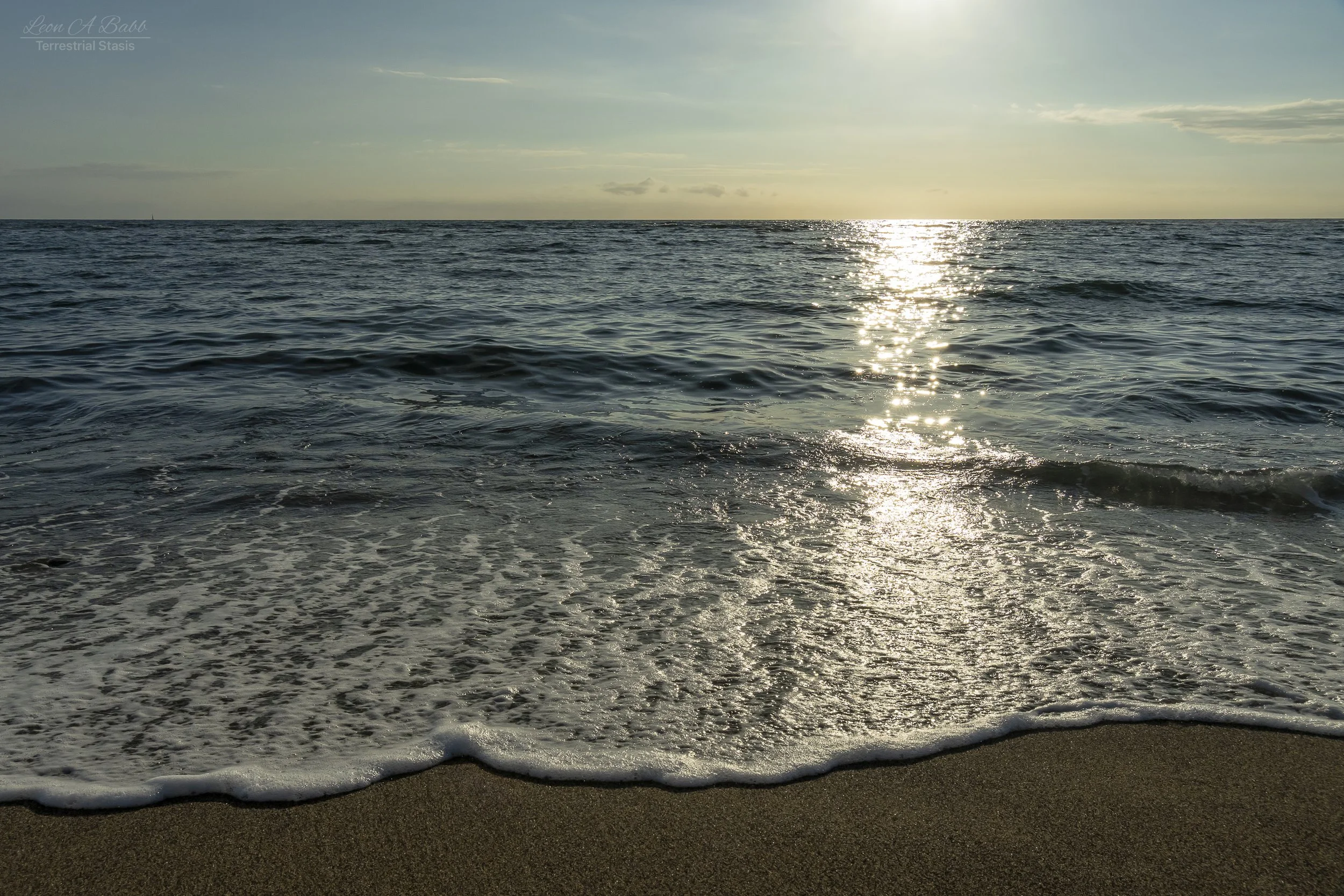 Sunset over the ocean with gentle waves lapping a sandy beach