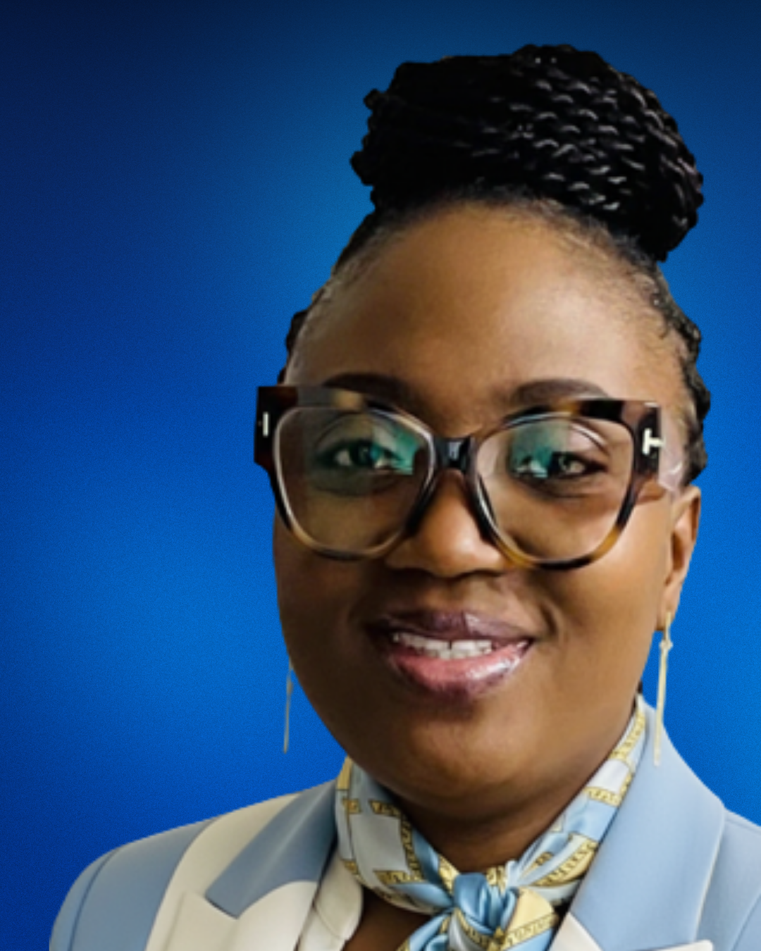 Picture of Yemi wearing a light blue suit, scarf, and classes, smiling at the camera.