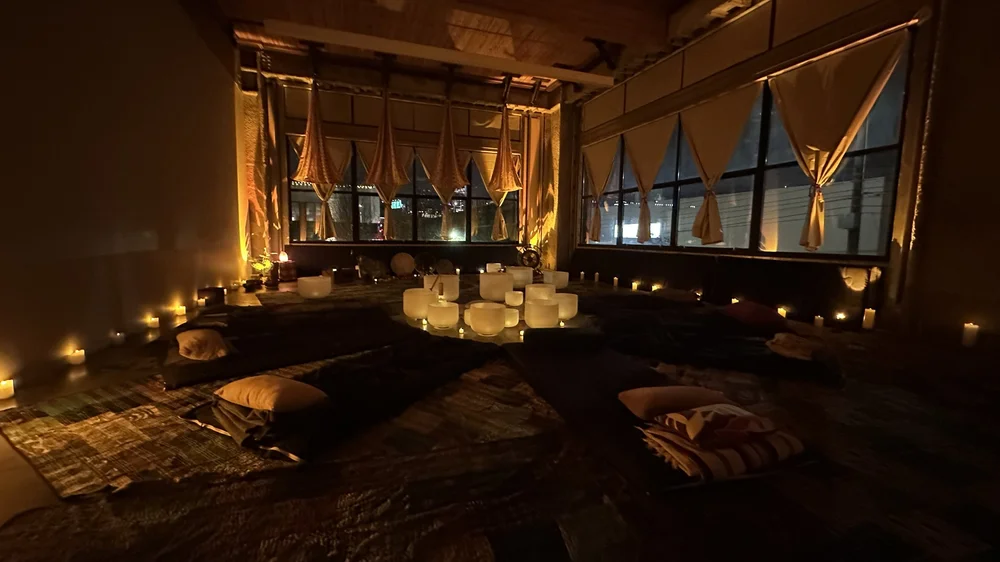 A candlelit Aloka pop-up: tall windows, crystal bowls on the floor, mats laid out for a session