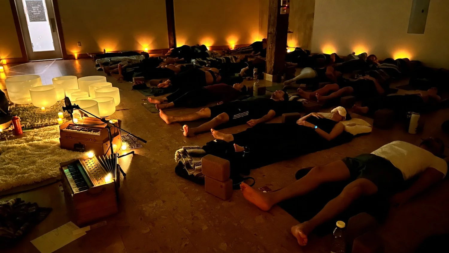 A candlelit Aloka sound bath at Wild Reed Yoga: people resting on mats, crystal bowls and a harmonium glowing by the wall