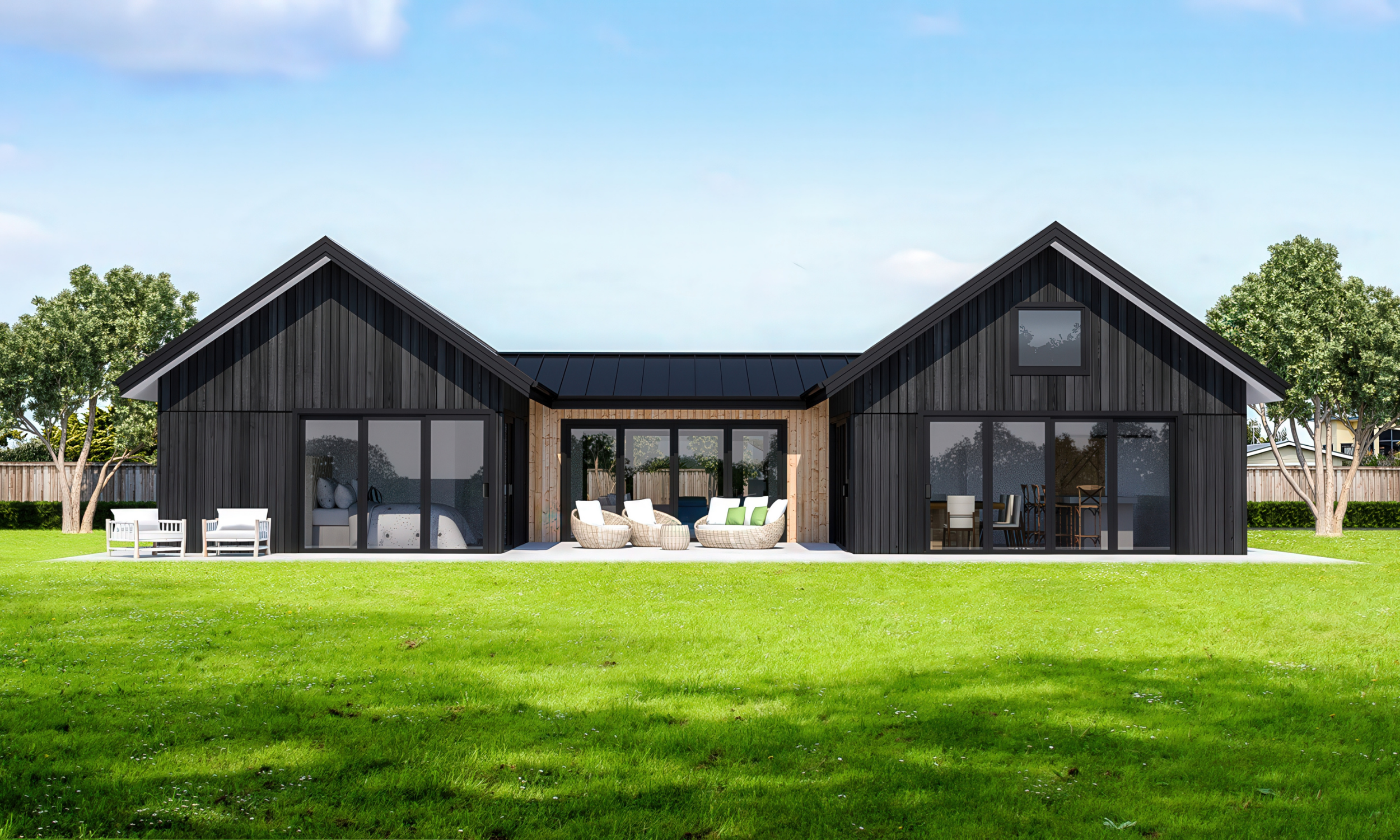 A modern black house with two gable roofs, large glass sliding doors, and an outdoor patio with white and green seating, set on a lush green lawn with trees in the background.