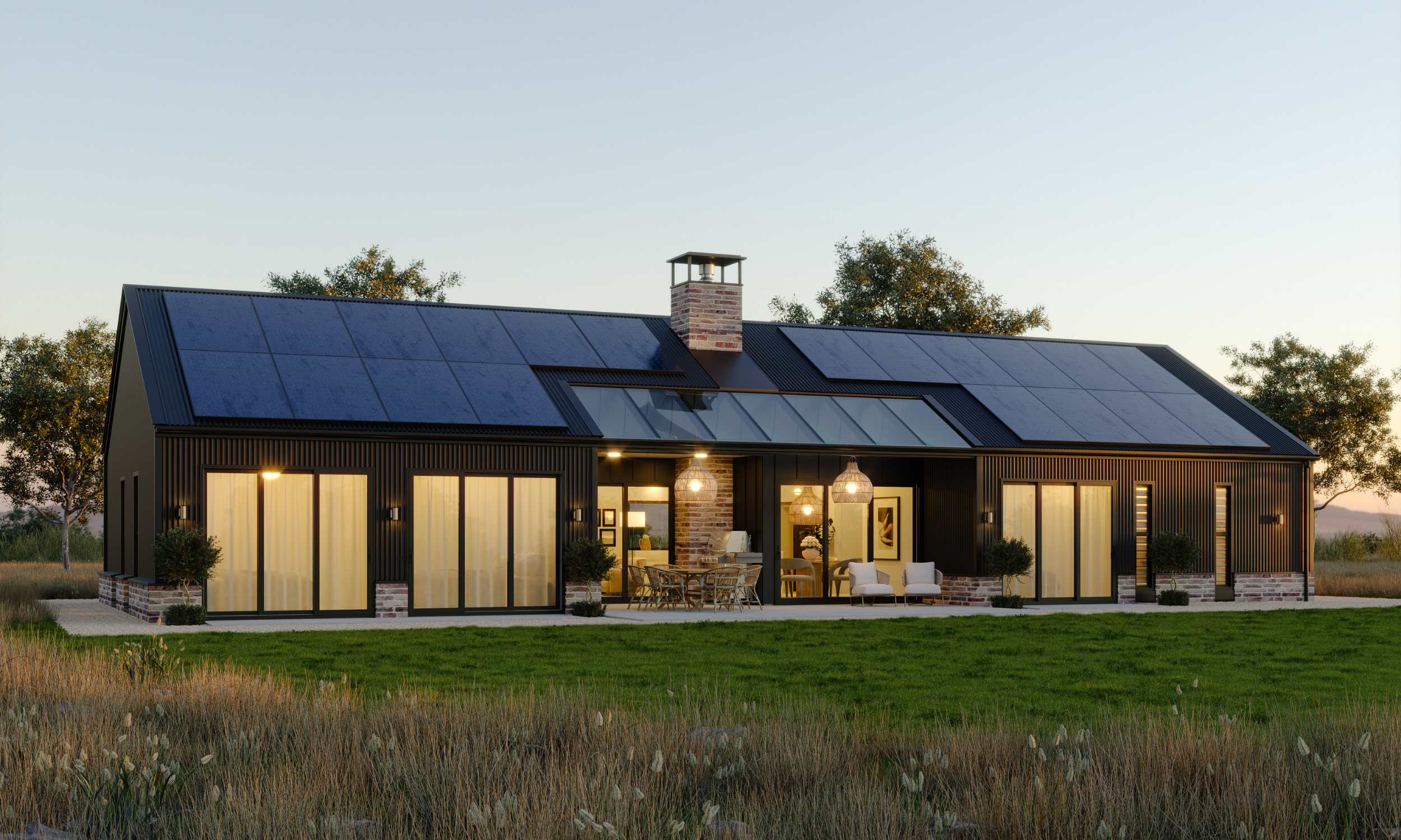 Modern house with black exterior, large glass sliding doors, solar panels on roof, outdoor patio with dining and sitting area, trees in background, lush lawn in foreground