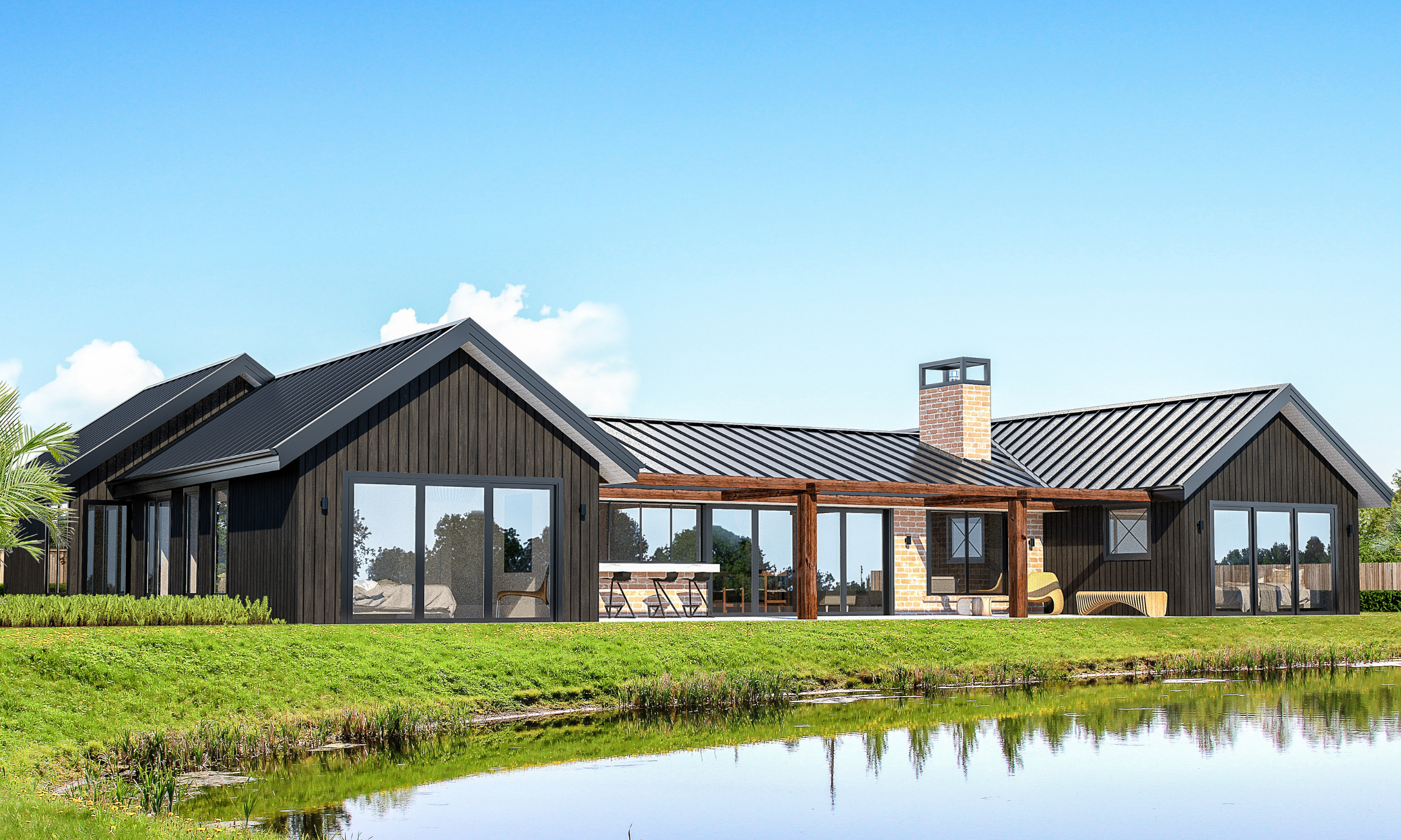 Modern house with black exterior, large glass windows, brick chimney, on a grassy bank near water, under blue sky with scattered clouds.