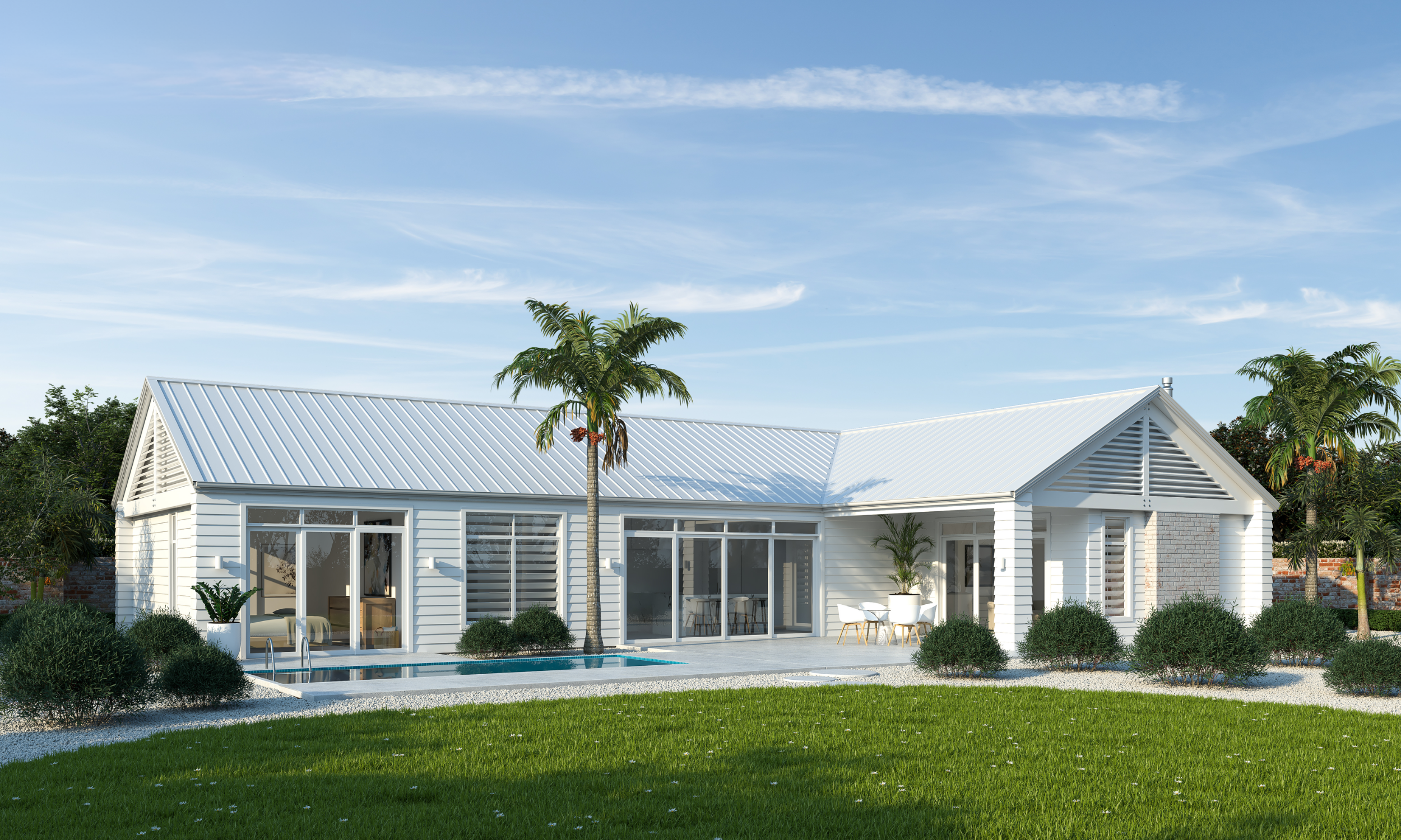 A modern white house with a metal roof, large windows, and an outdoor patio, surrounded by a green lawn, palm trees, and landscaped bushes under a blue sky.