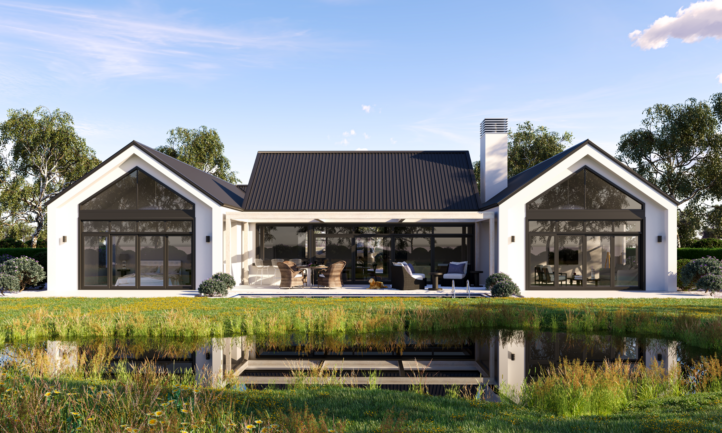 Modern house with large patio, outdoor furniture, and a pond in the foreground, surrounded by trees and blue sky.