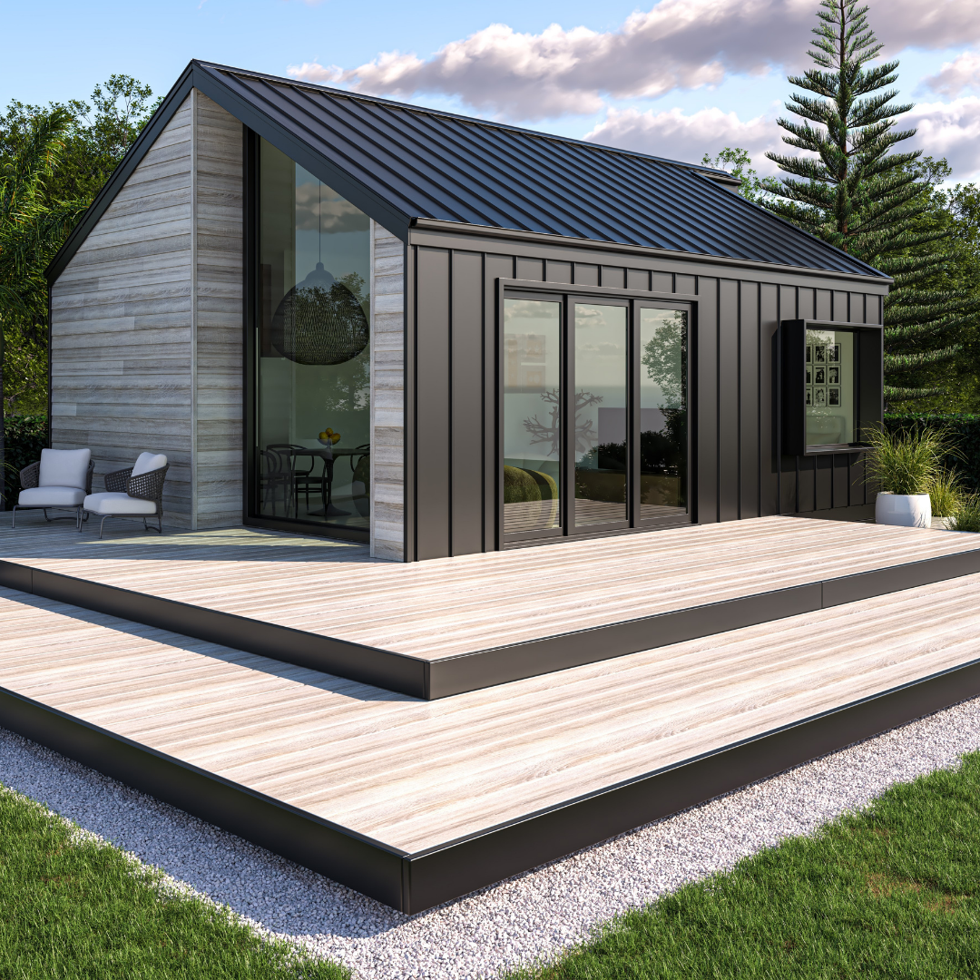 Modern house with black metal siding and large glass sliding doors on a wooden deck, surrounded by greenery and trees.