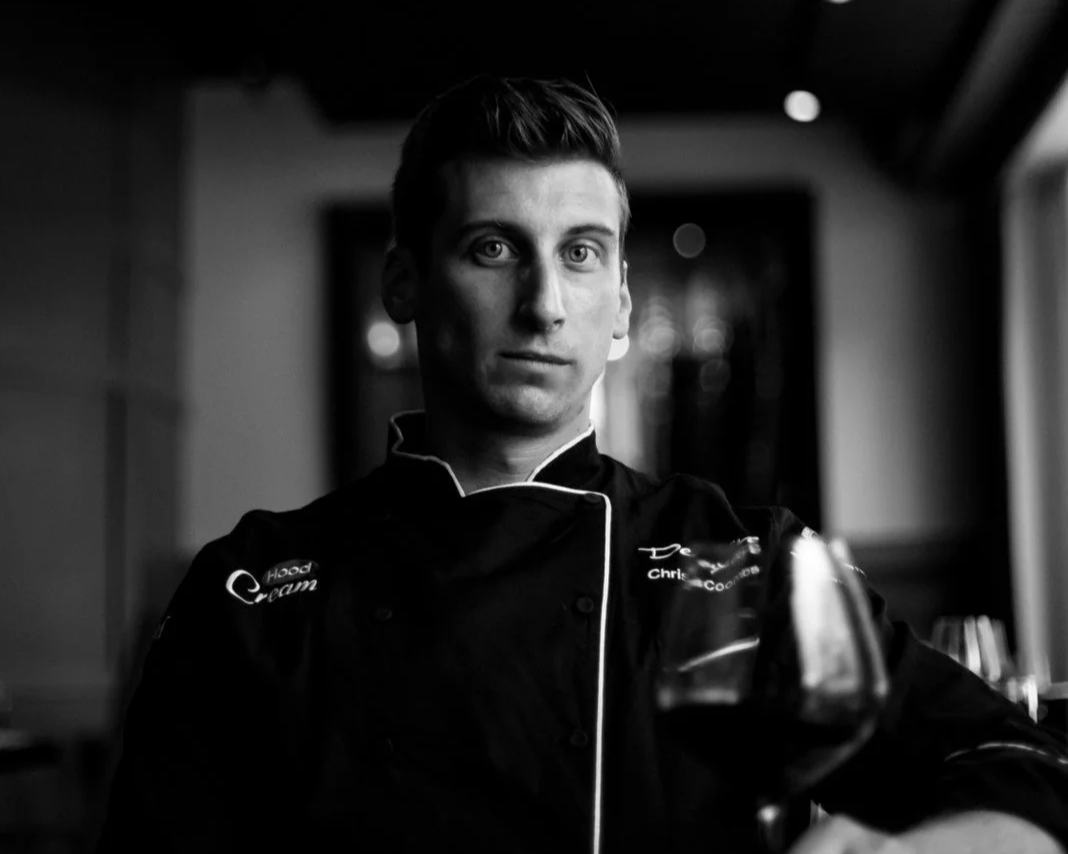 A man in a chef's uniform holding a glass of wine indoors.