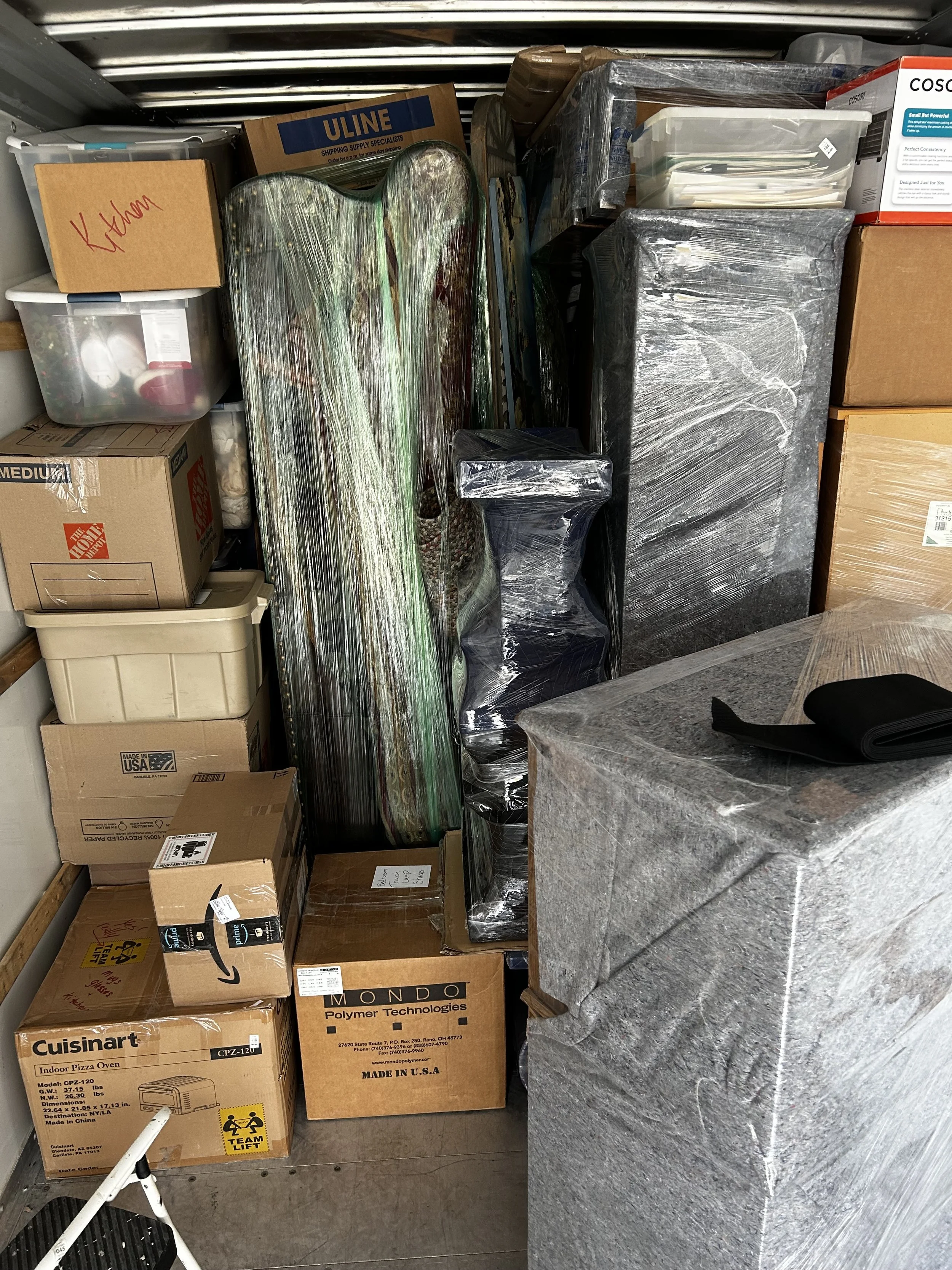 Three people inside a moving truck, loading or organizing boxes towards the front of the truck.