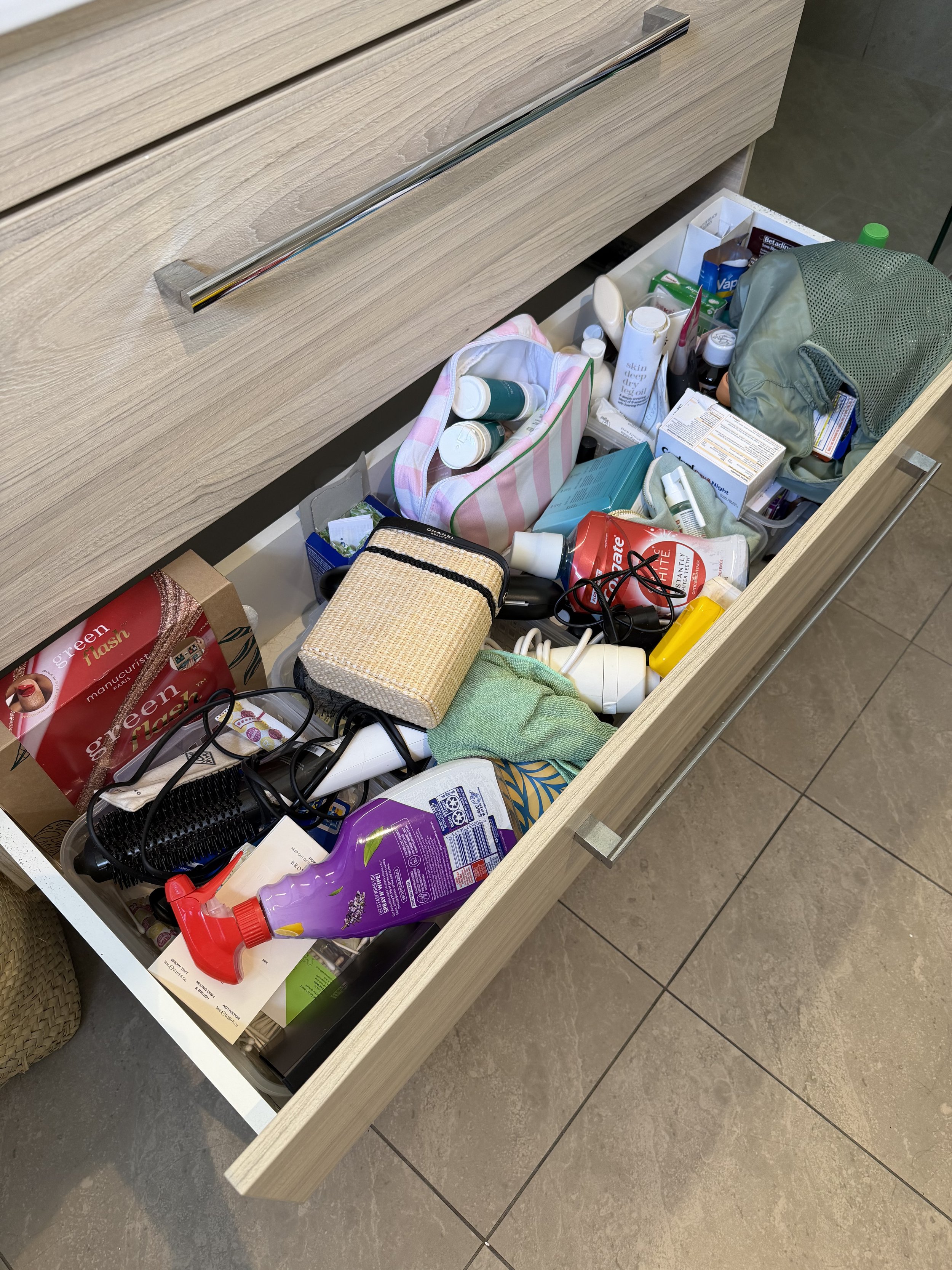Before bathroom drawer transformation showing cluttered beauty products, toiletries and everyday essentials in need of organising.