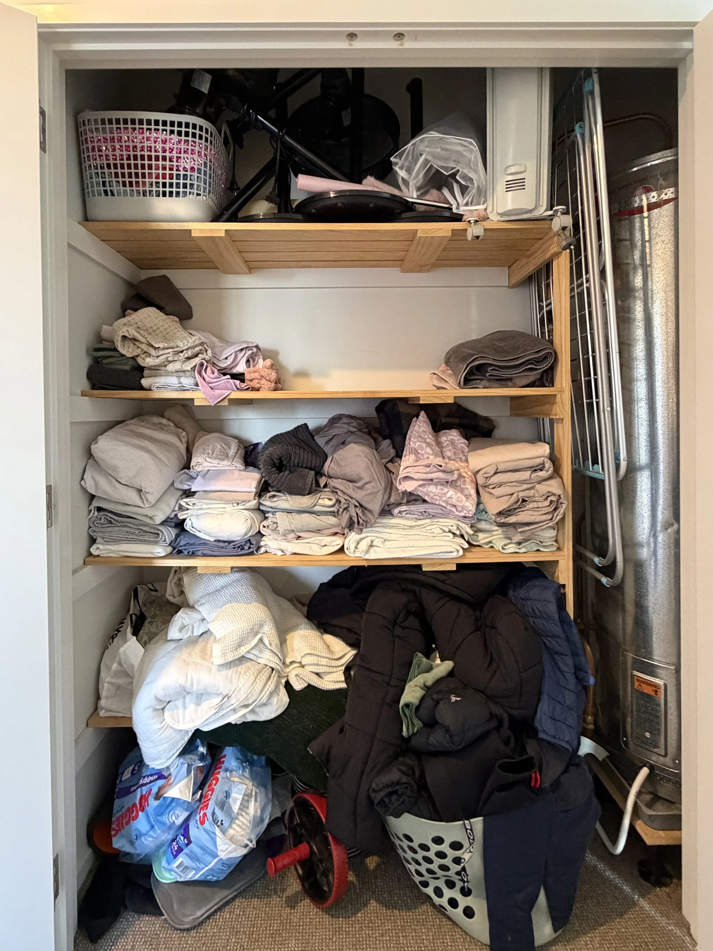 Before home organising, a cluttered linen cupboard with overflowing towels, bedding and household items stacked across shelves.