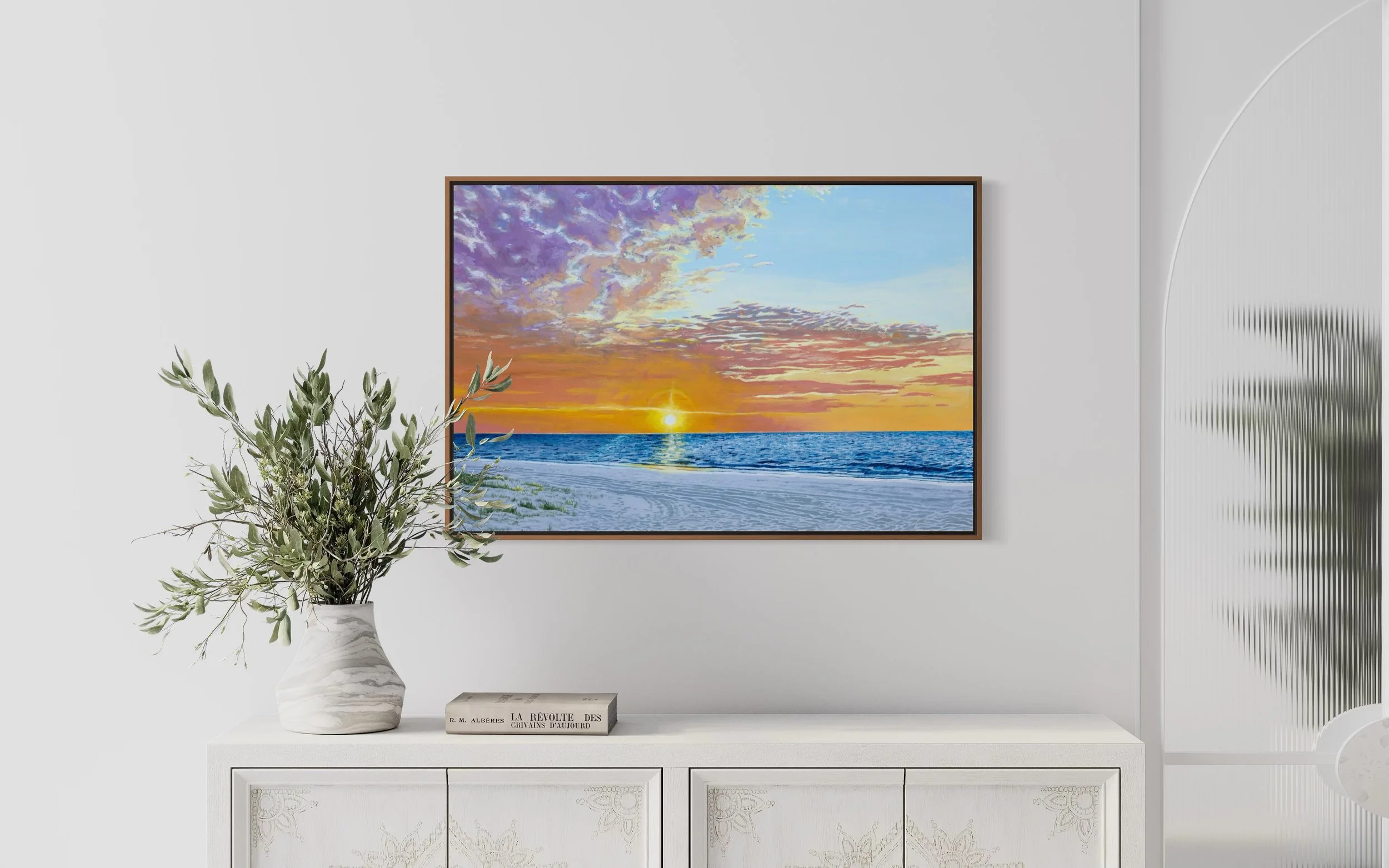 A framed painting of Fraser Island (K'gari) picturing a sunset over the ocean hangs on a white wall in a minimalistic room. it features bright colourful clouds with pink, yellow and purples