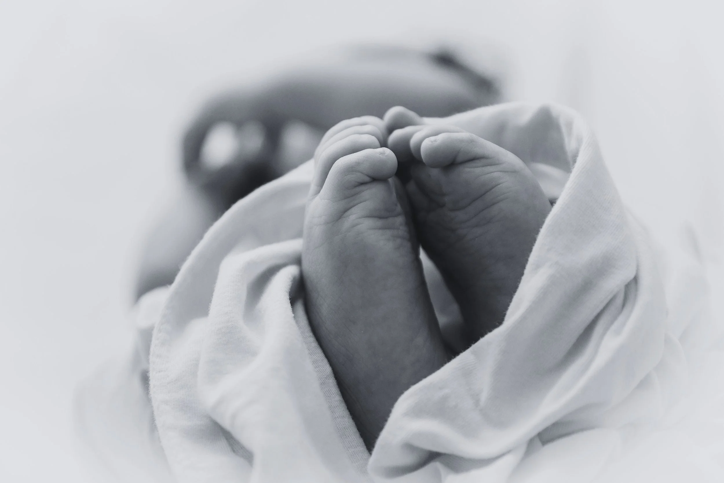 Close-up of a baby's small hand grasping an adult's finger, in black and white.