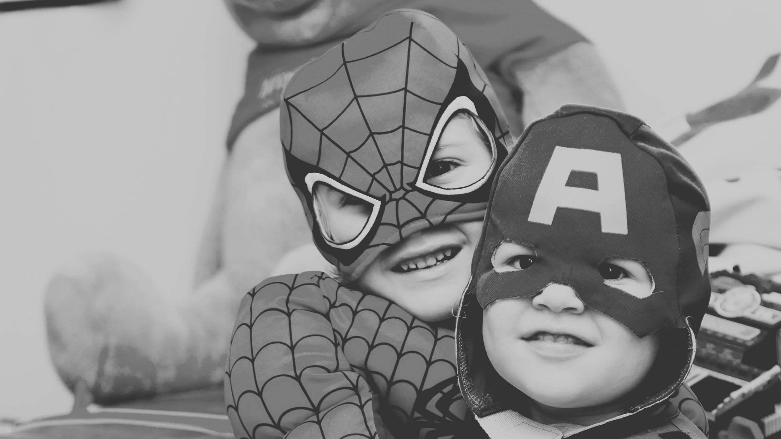 Two children wearing Spiderman and Captain America masks hugging each other.