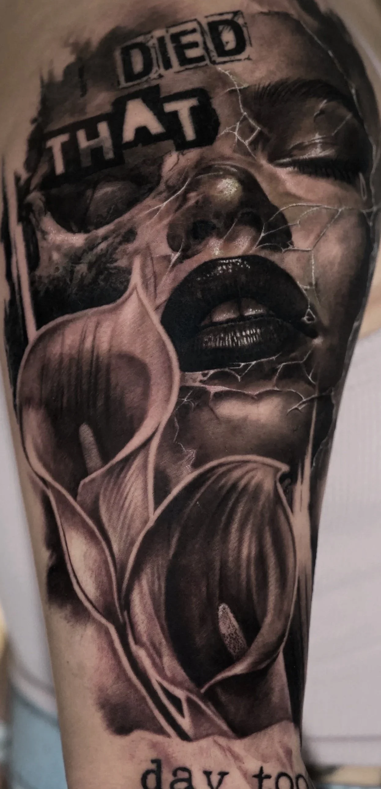 Tattoo of a woman's face with cracked glass effect and the words "DIED THAT DAY TOO" above her head, on a person's arm. A tattoo that expresses grief. Tattoo done by Allan Mandi realism tattoo Artist from Knoxville Tennessee