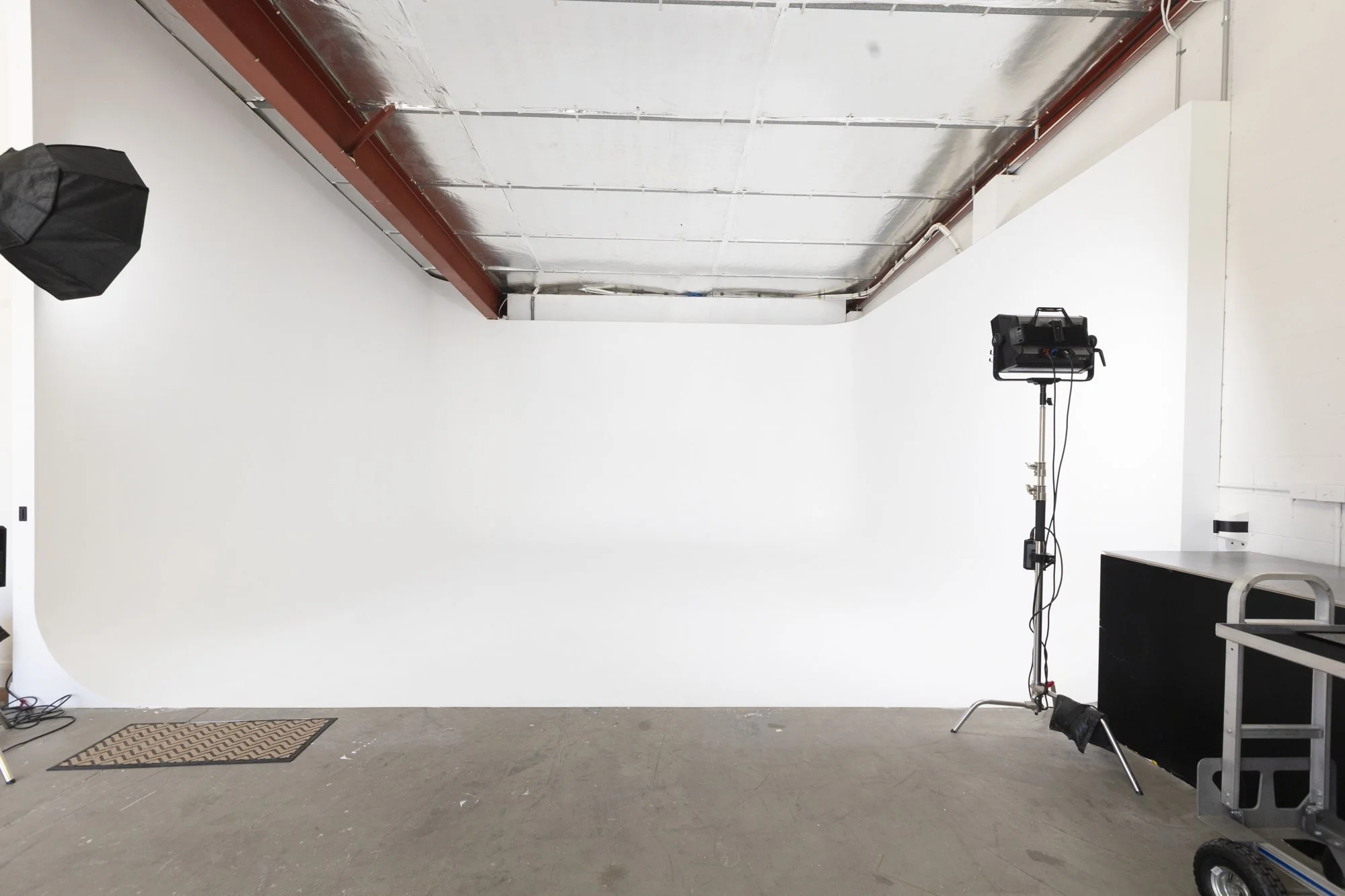 A photography studio with a large white backdrop, studio lights on stands, and equipment on a cart, set up for photoshoot.