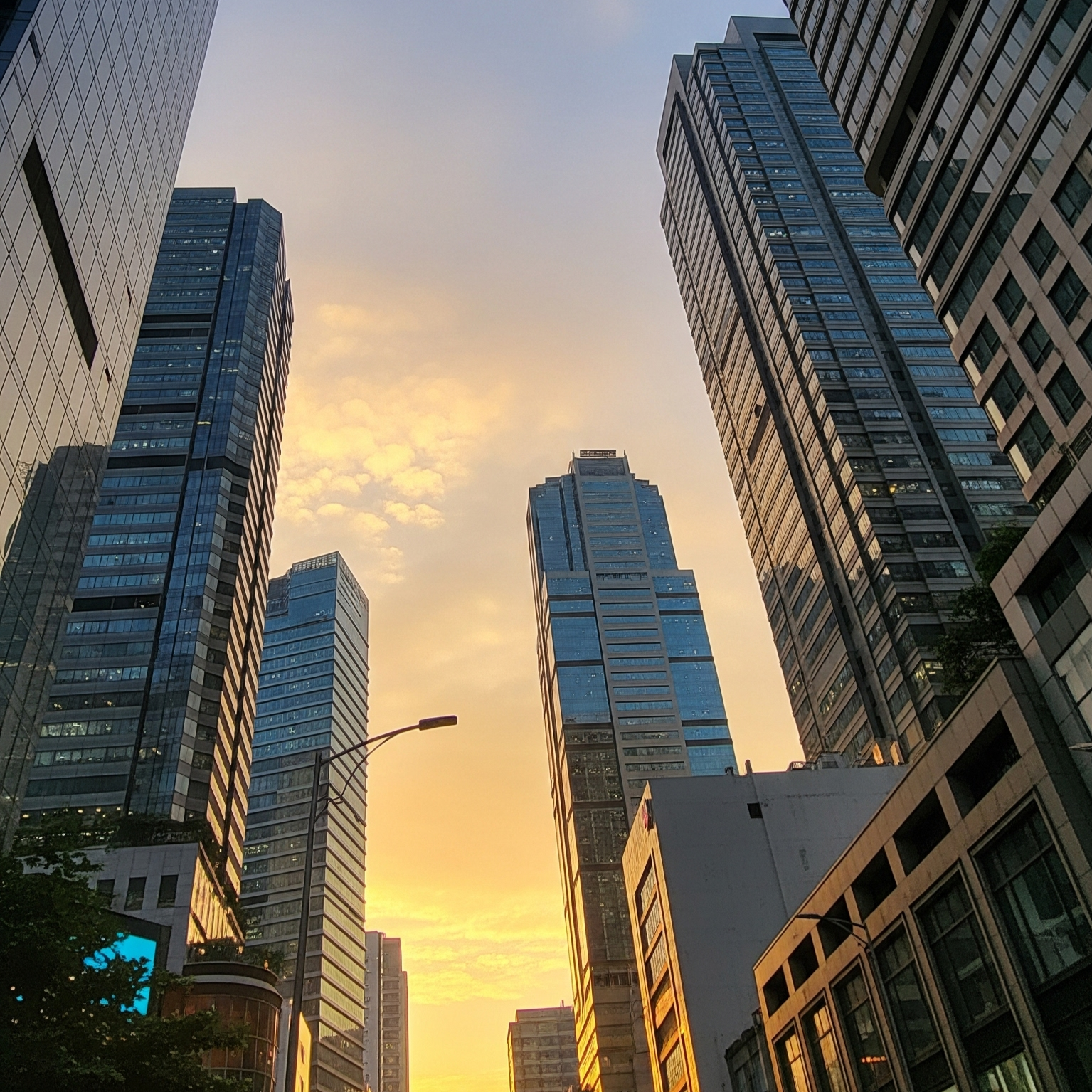 Tall modern skyscrapers in a city at sunset with a colorful sky and reflections on glass buildings.