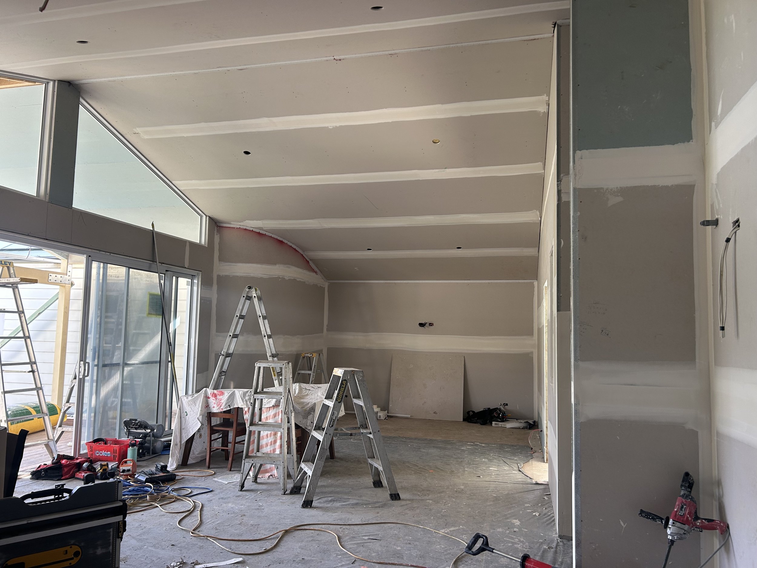 Room under construction with ladders, tools, and drywall in progress.