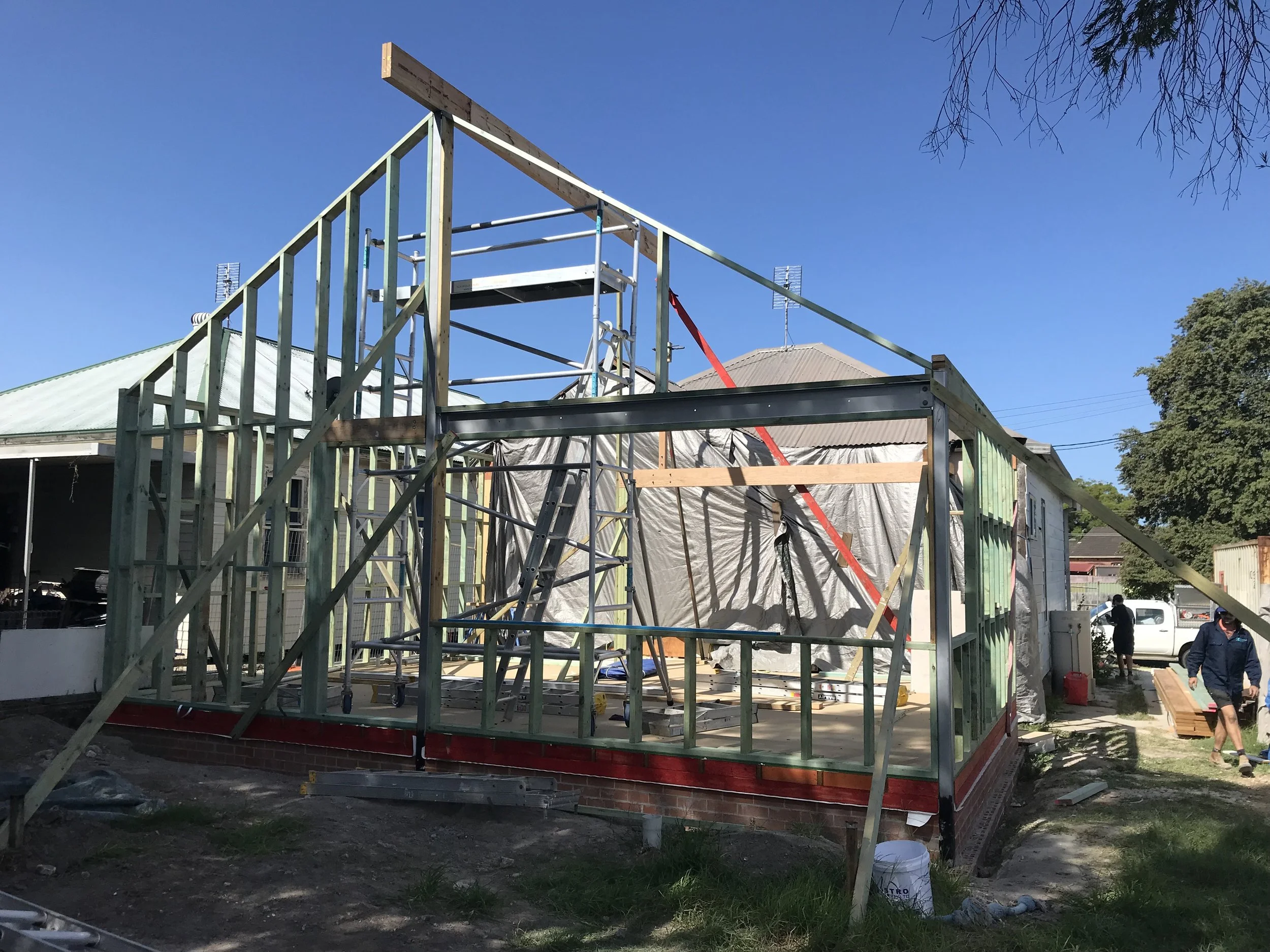 Construction of a house with a wooden frame and scaffolding on a clear day.