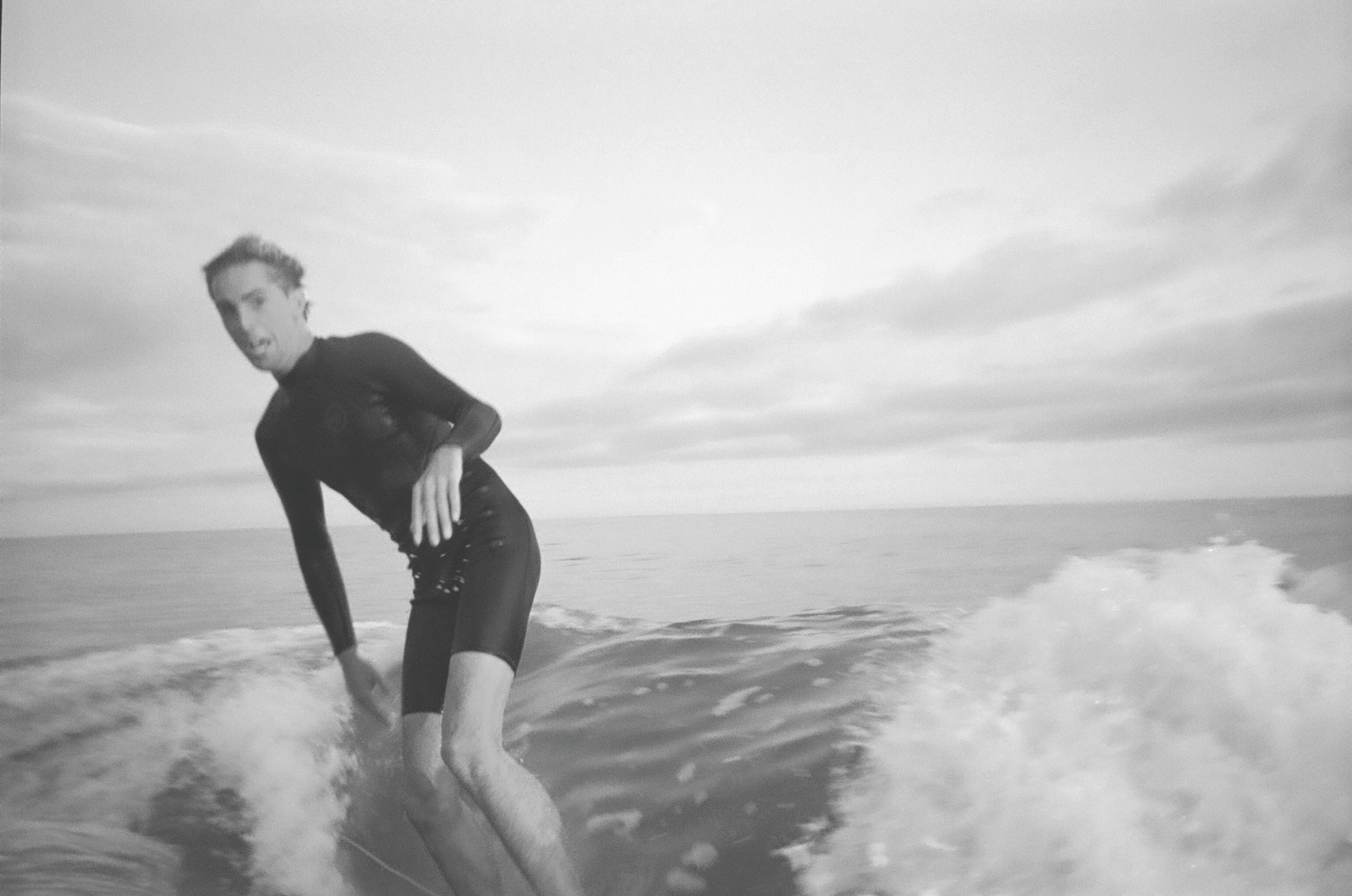 A person surfing on a wave in the ocean during cloudy weather, wearing a wetsuit.