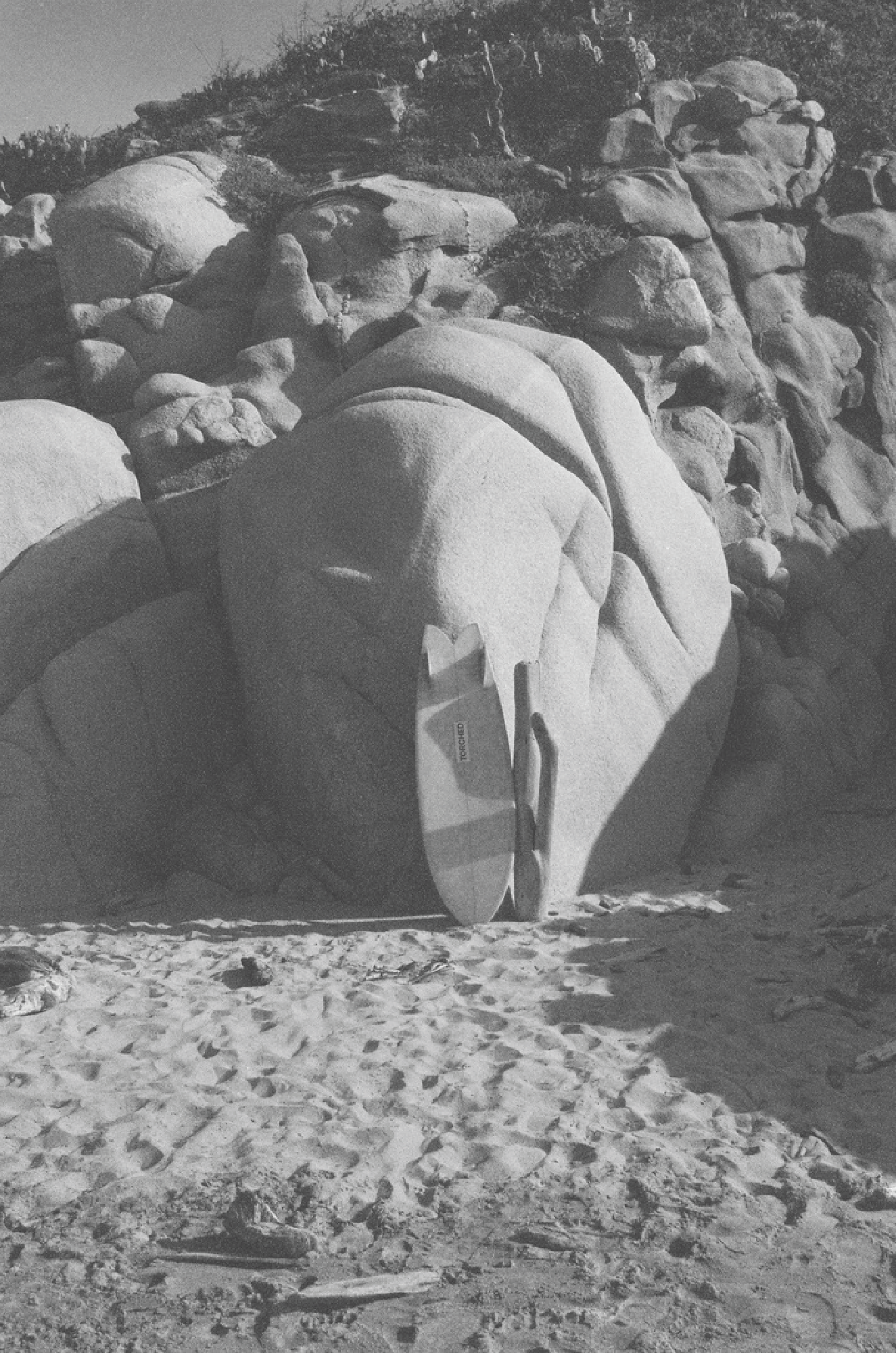 surfboard resting against rocks on a sandy beach with rock formations in the background in mexico