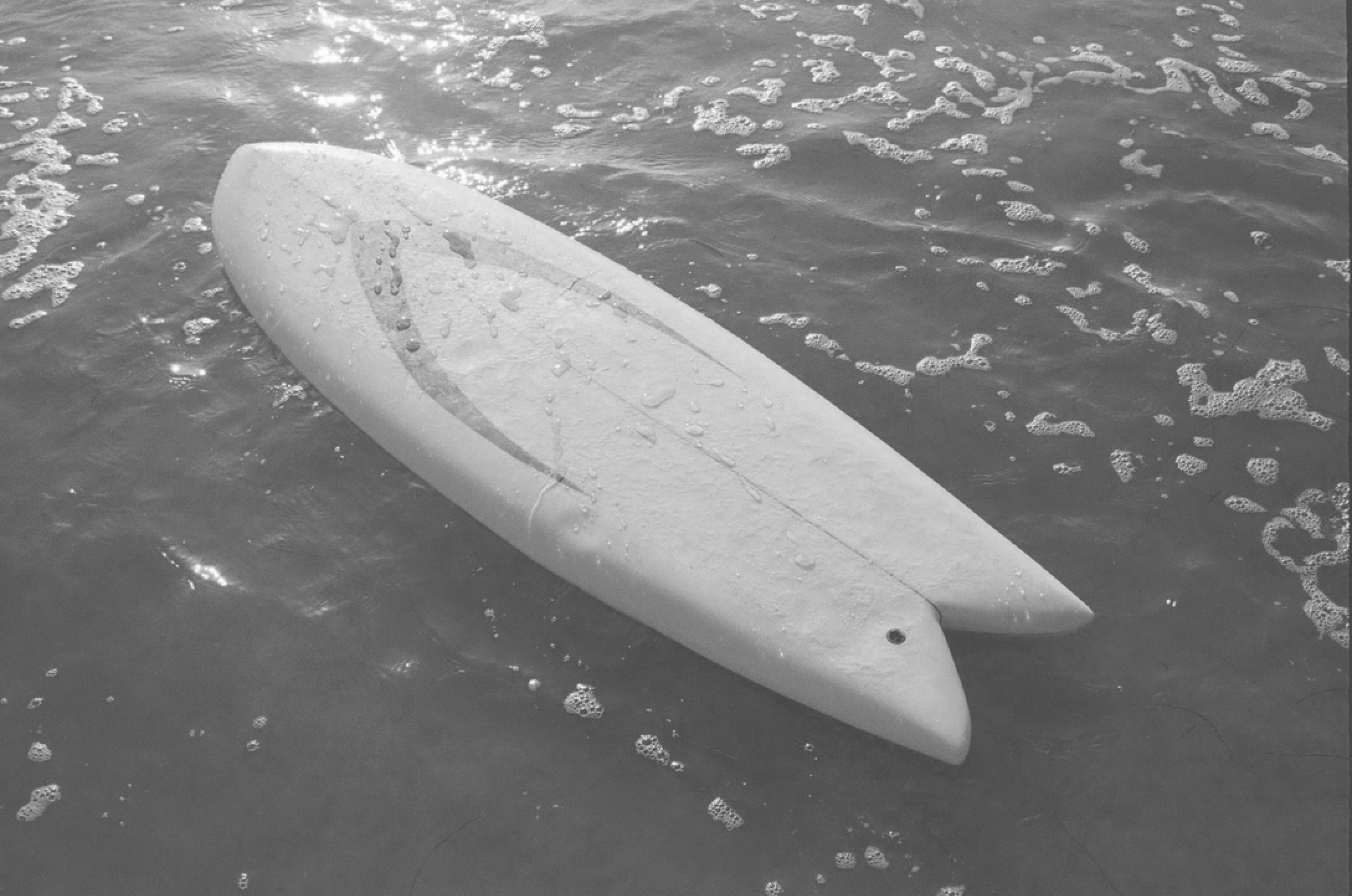 A surfboard lying on the wet sand, with water droplets on its surface.