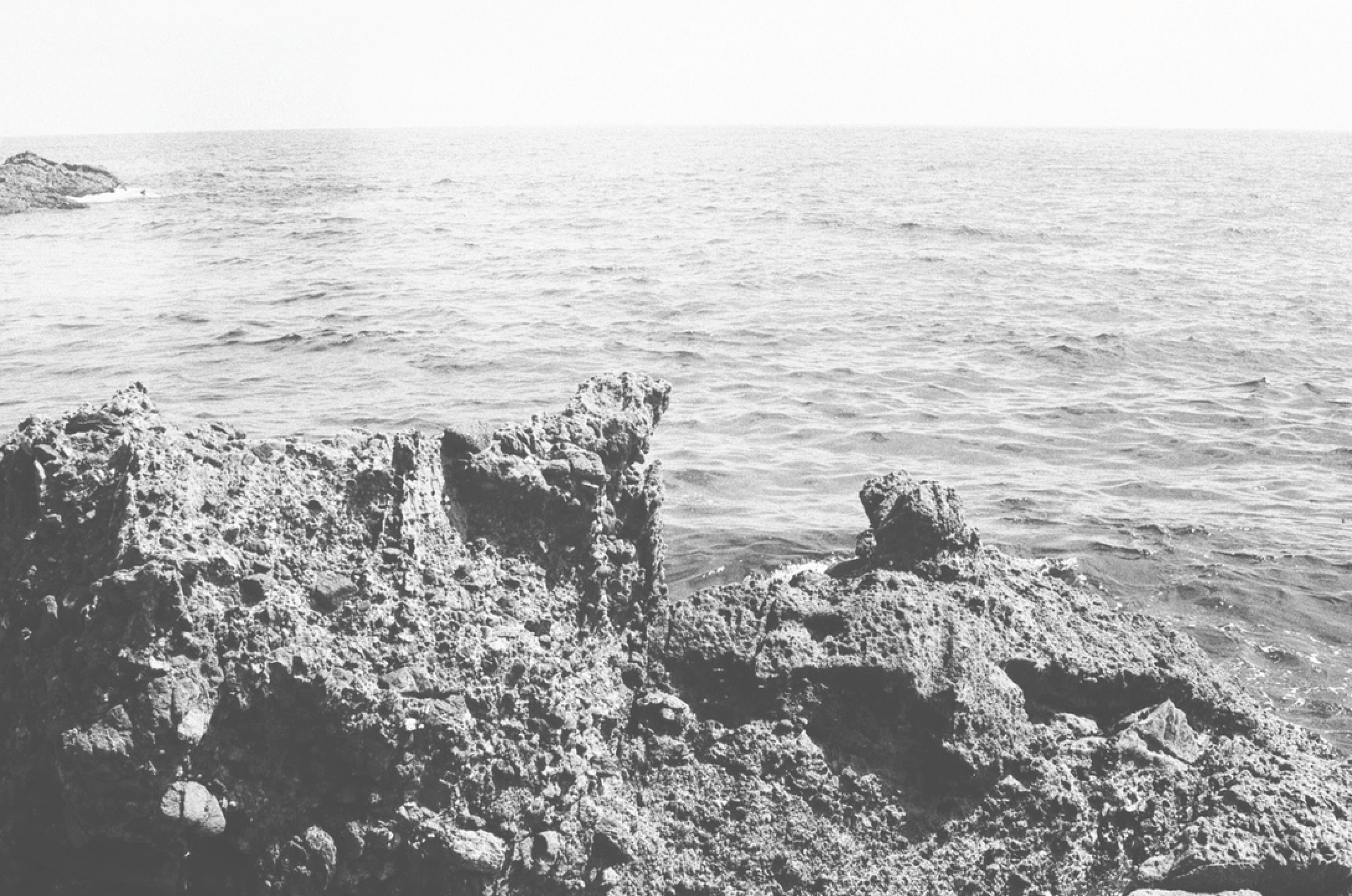 Black and white photograph of rocky shoreline with the ocean in the background.