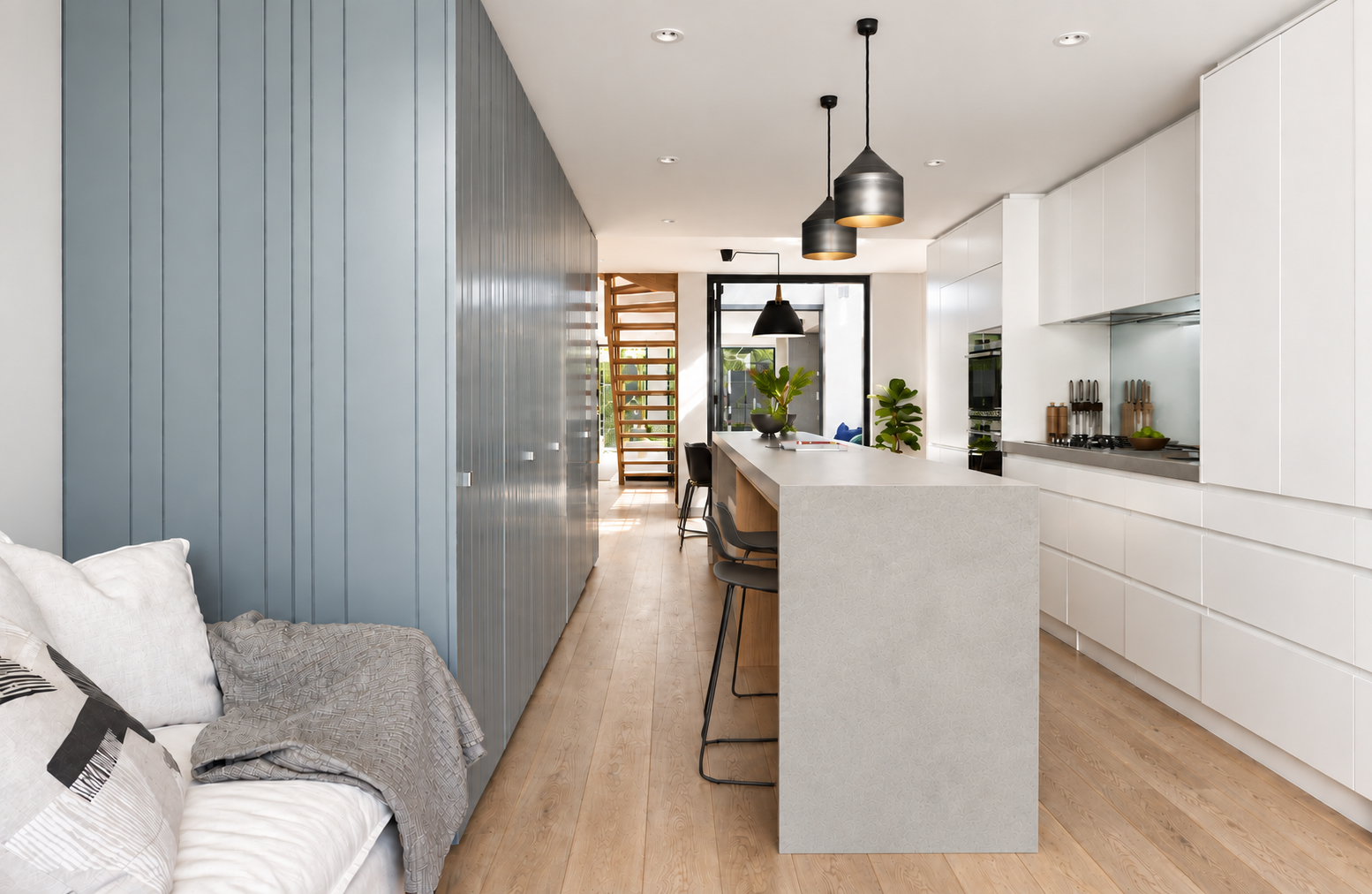 Modern open-concept kitchen with white cabinetry, kitchen island, black pendant lights, and wooden flooring, with a living area visible in the background.