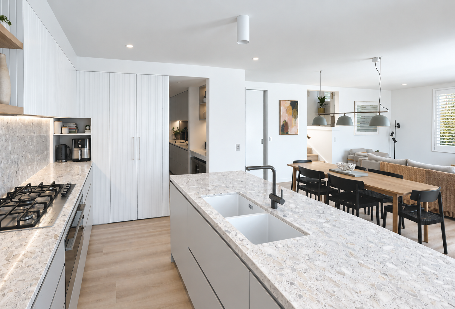 Modern open-plan kitchen and dining area with terrazzo countertops, black chairs, and white walls.