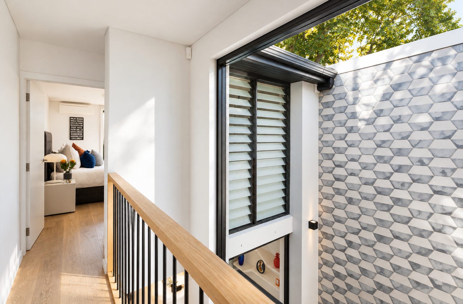 Interior view of a modern home hallway with white walls, a wooden railing, a black window with louvered blinds, and a patterned marble wall.