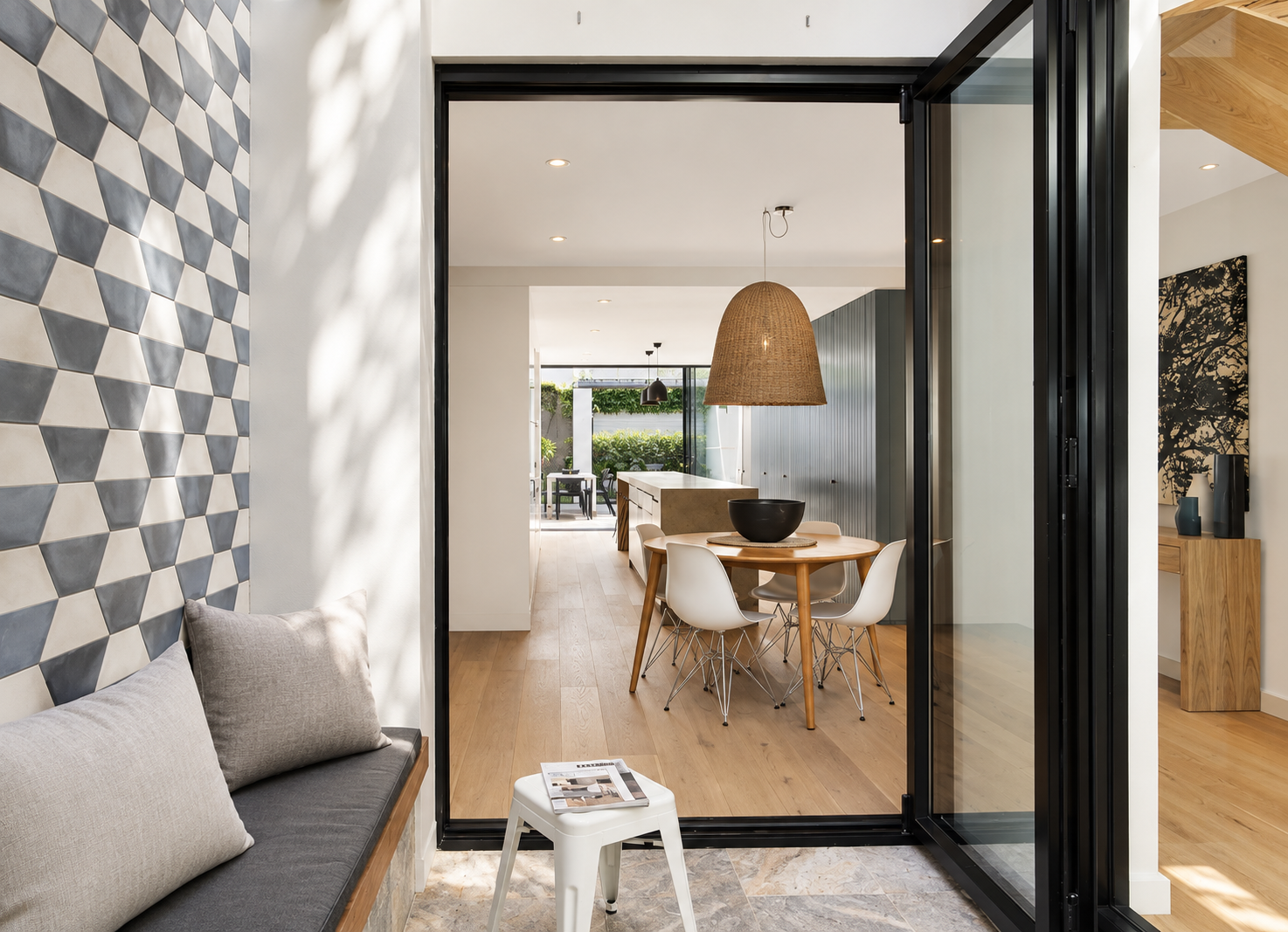 Modern open-concept kitchen and dining area with light wood flooring, white walls, and black accents, featuring a round wooden table with four white chairs and a large woven pendant light overhead.