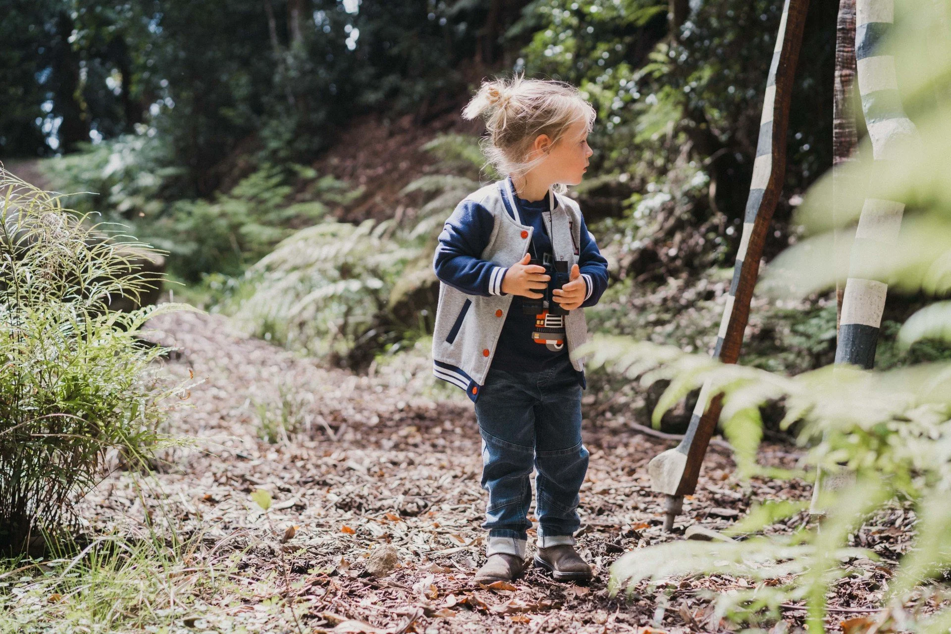 Young boy standing on a forest trail holding binoculars.