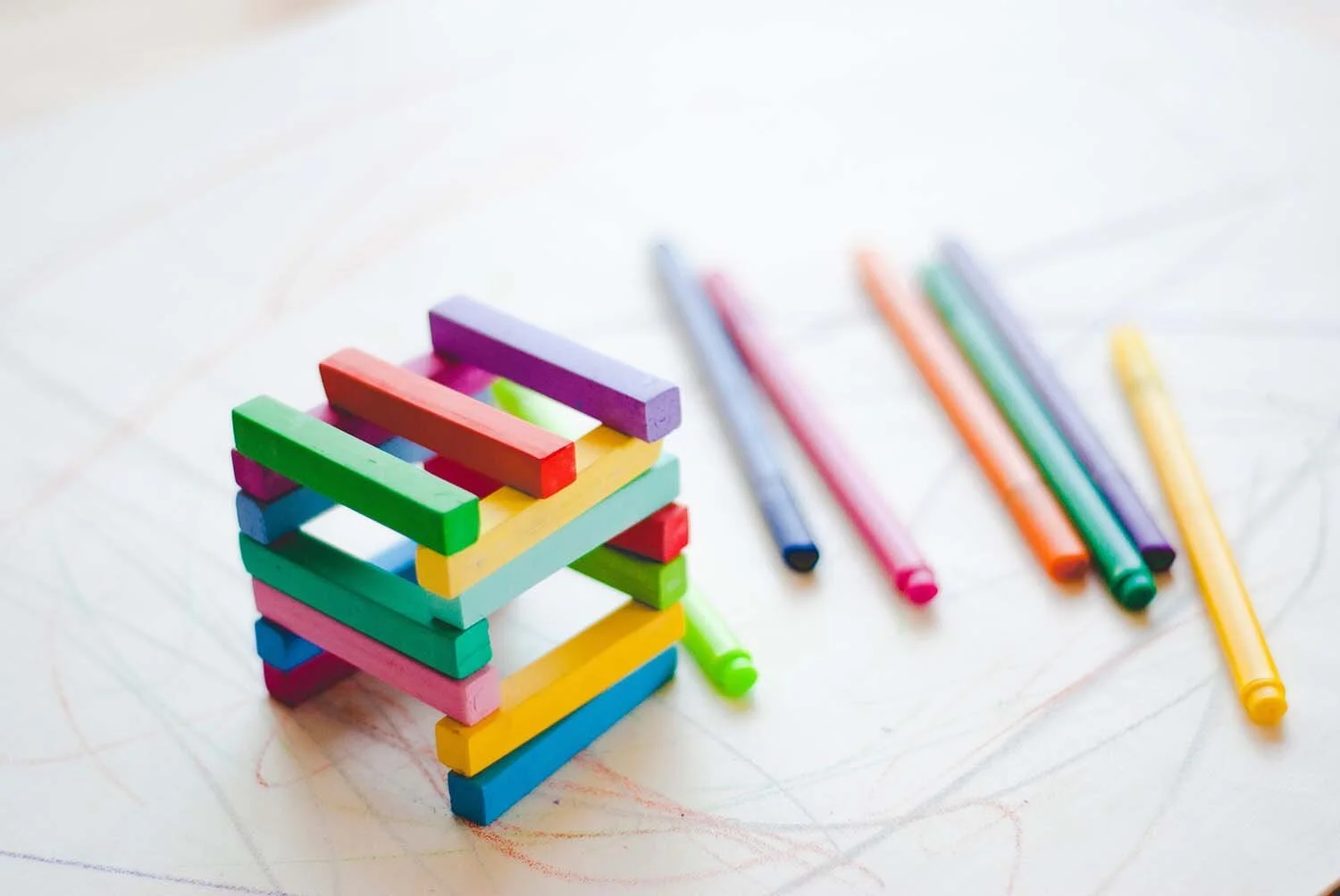 Colorful wooden sticks arranged in a 3D cube shape with crayons and markers on a white surface