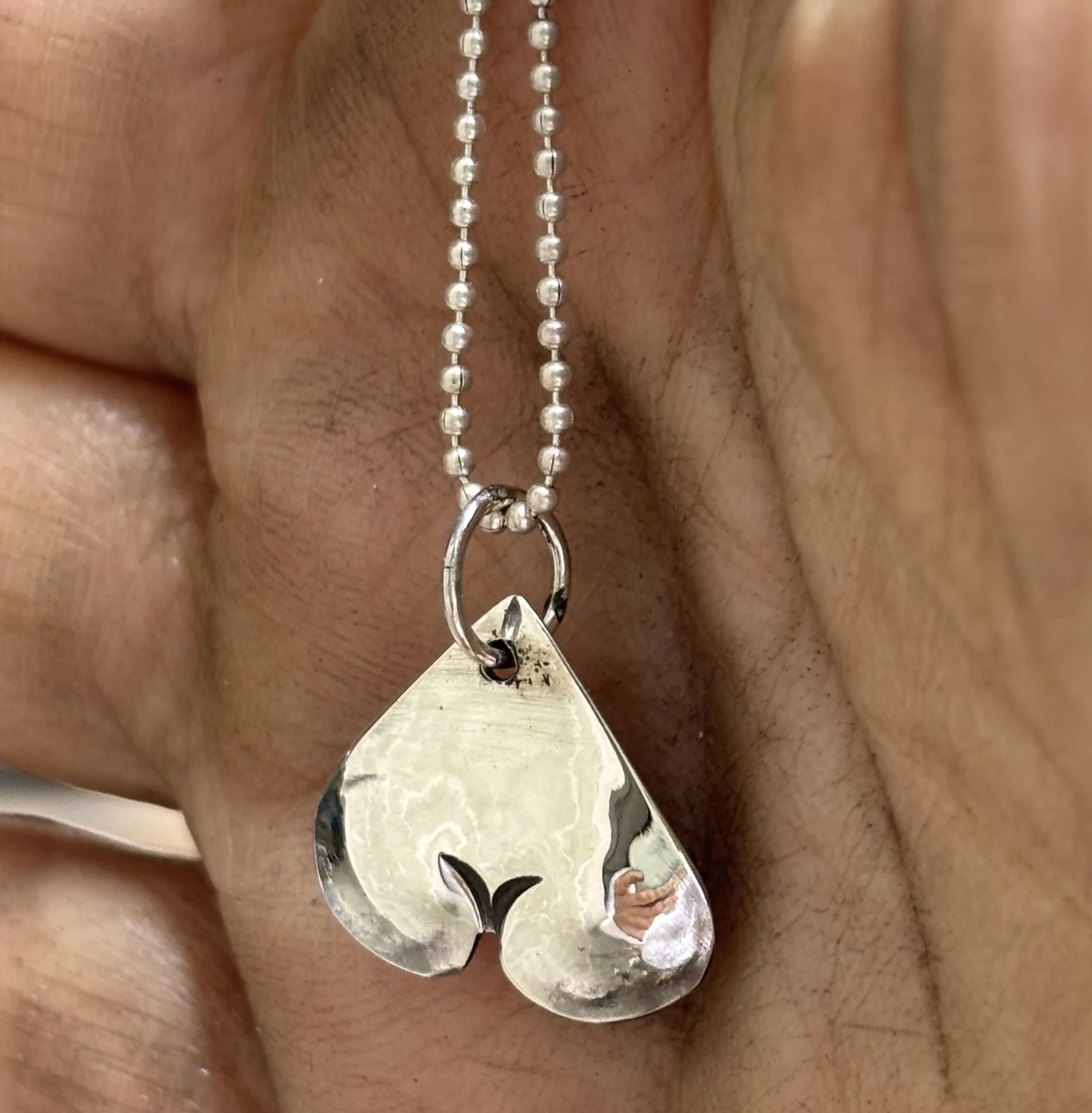 A close-up of a person's ear adorned with a silver ball chain necklace and a silver pendant.