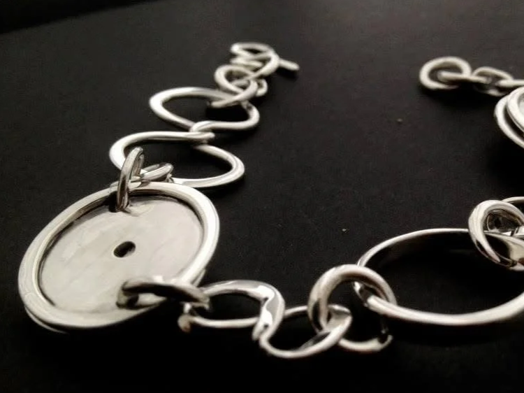 Close-up of a silver chain with a round, flat pendant against a black background.