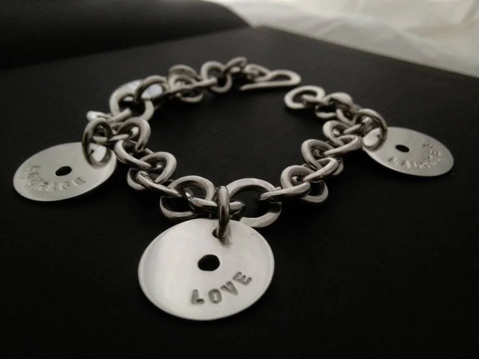 Silver charm bracelet with three round pendants engraved with the words "LOVE" and a hole in the center, resting on a black surface.