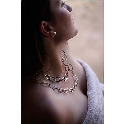 Close-up of a woman with jewelry, wearing a pearl earring and layered chain necklaces, draped in a soft fabric, looking upward.